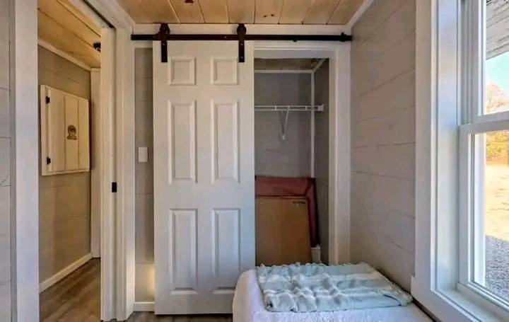 Cozy room with a rustic barn door closet, soft natural light from a large window, and a neatly folded blanket on a bed, creating a serene atmosphere.