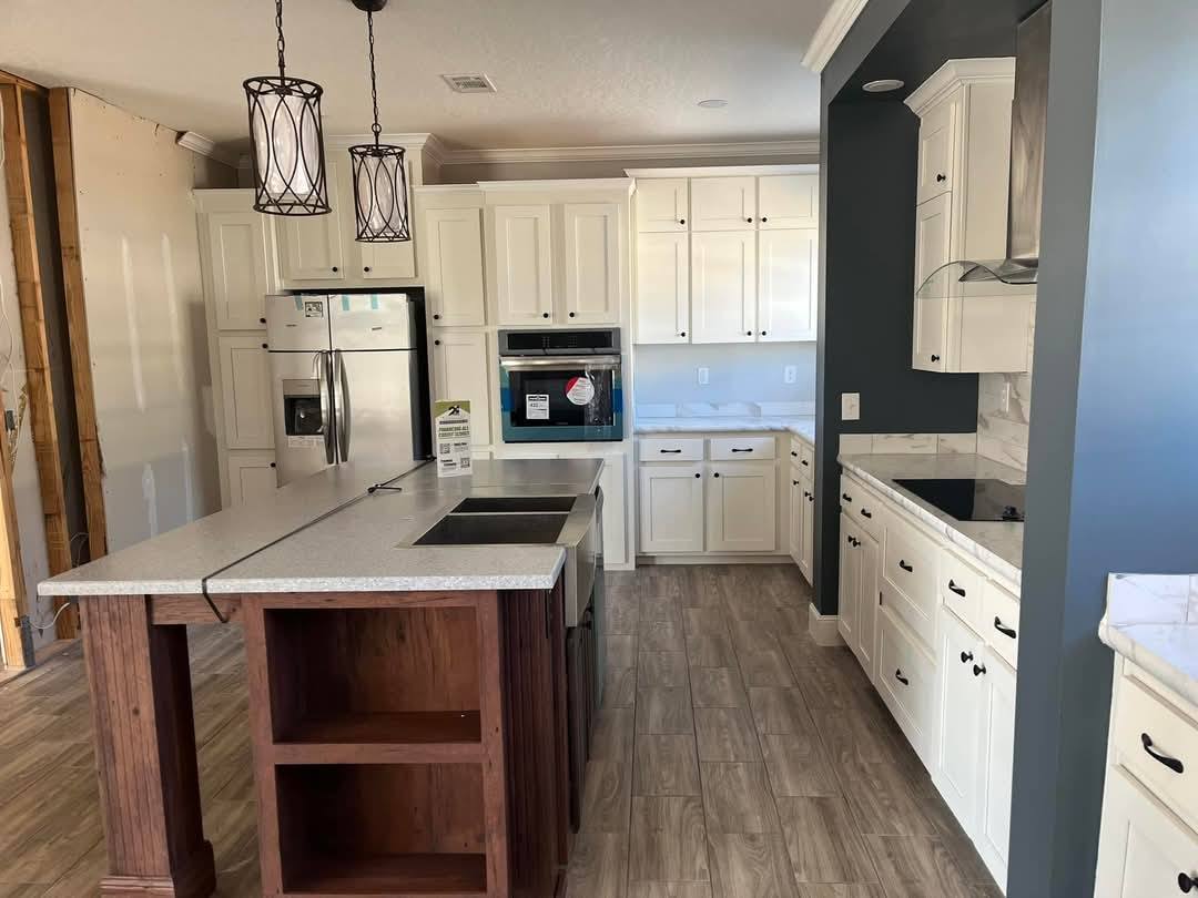 Modern kitchen with white cabinets, stainless steel appliances, and wood island. Pendant lights hang above. Light wood flooring adds warmth.