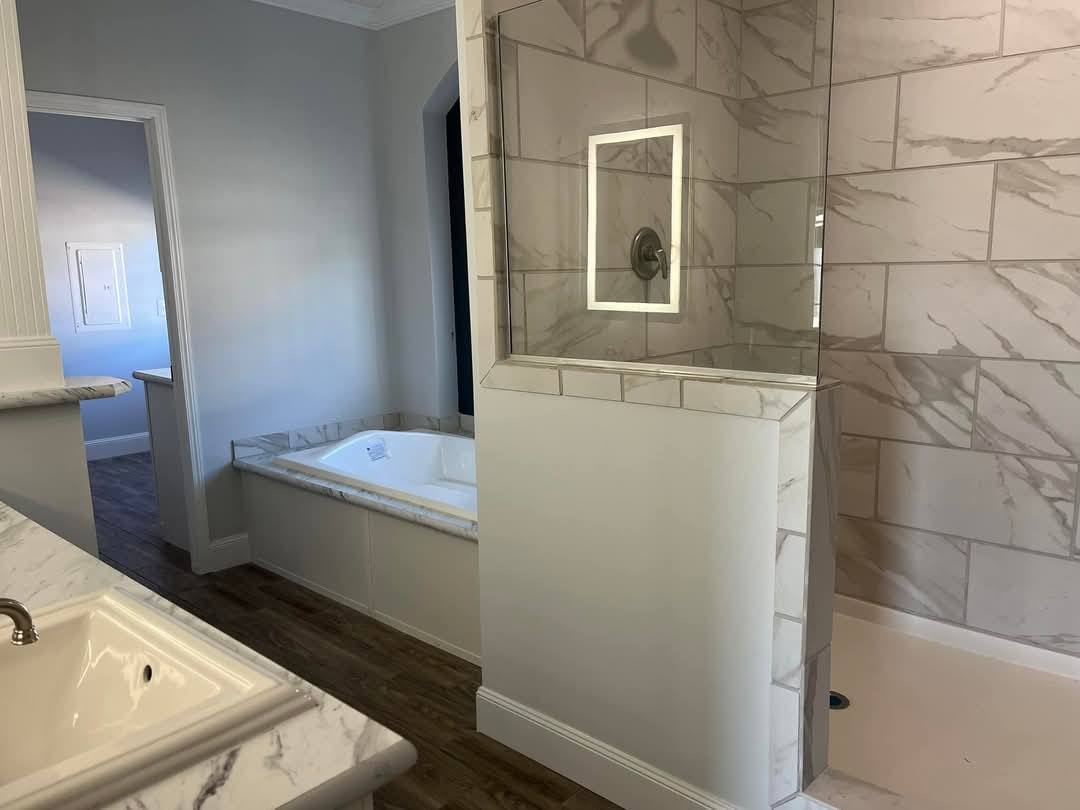 Modern bathroom with marble tiles, featuring a glass-enclosed shower and a corner bathtub. Wood flooring adds warmth to the sleek, stylish design.