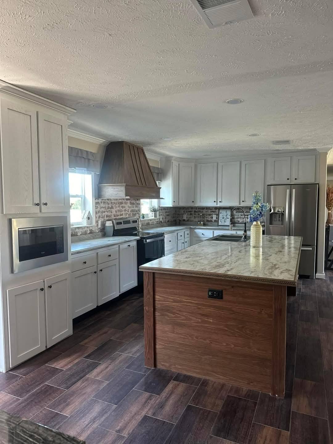 Spacious kitchen with white cabinets, brick backsplash, and a large island with a flower vase. Stainless steel appliances and wooden accents.