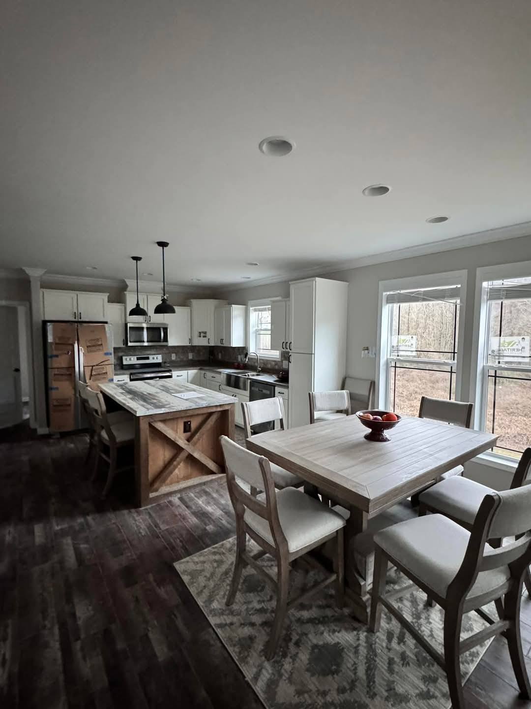 Spacious modern kitchen with white cabinetry, stainless steel appliances, and a wooden island. Dining table with six chairs, large windows, warm ambiance.