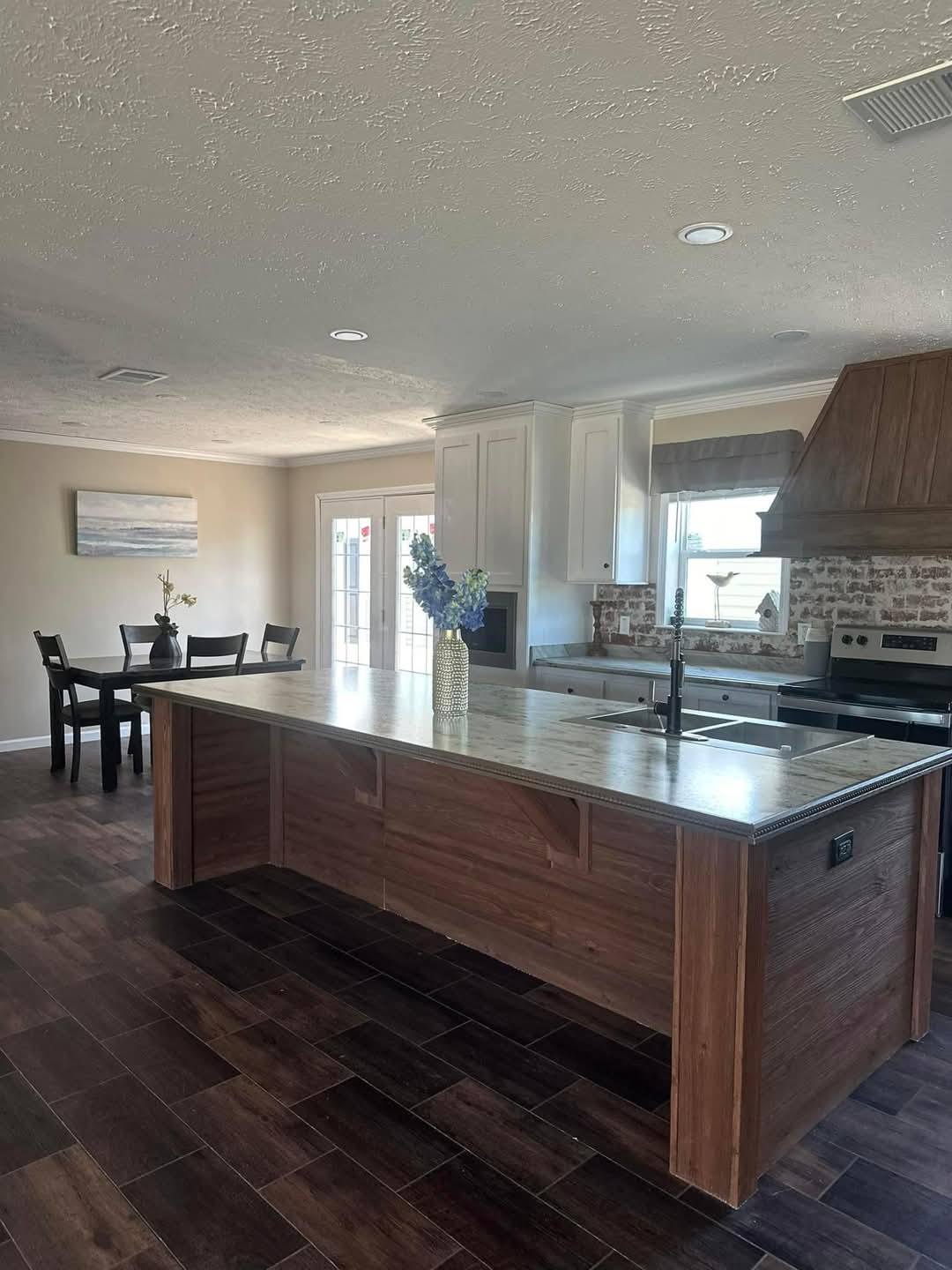 Spacious kitchen with a large wooden island, marble countertop, and a vase of flowers. Modern appliances and brick backsplash add a cozy touch.