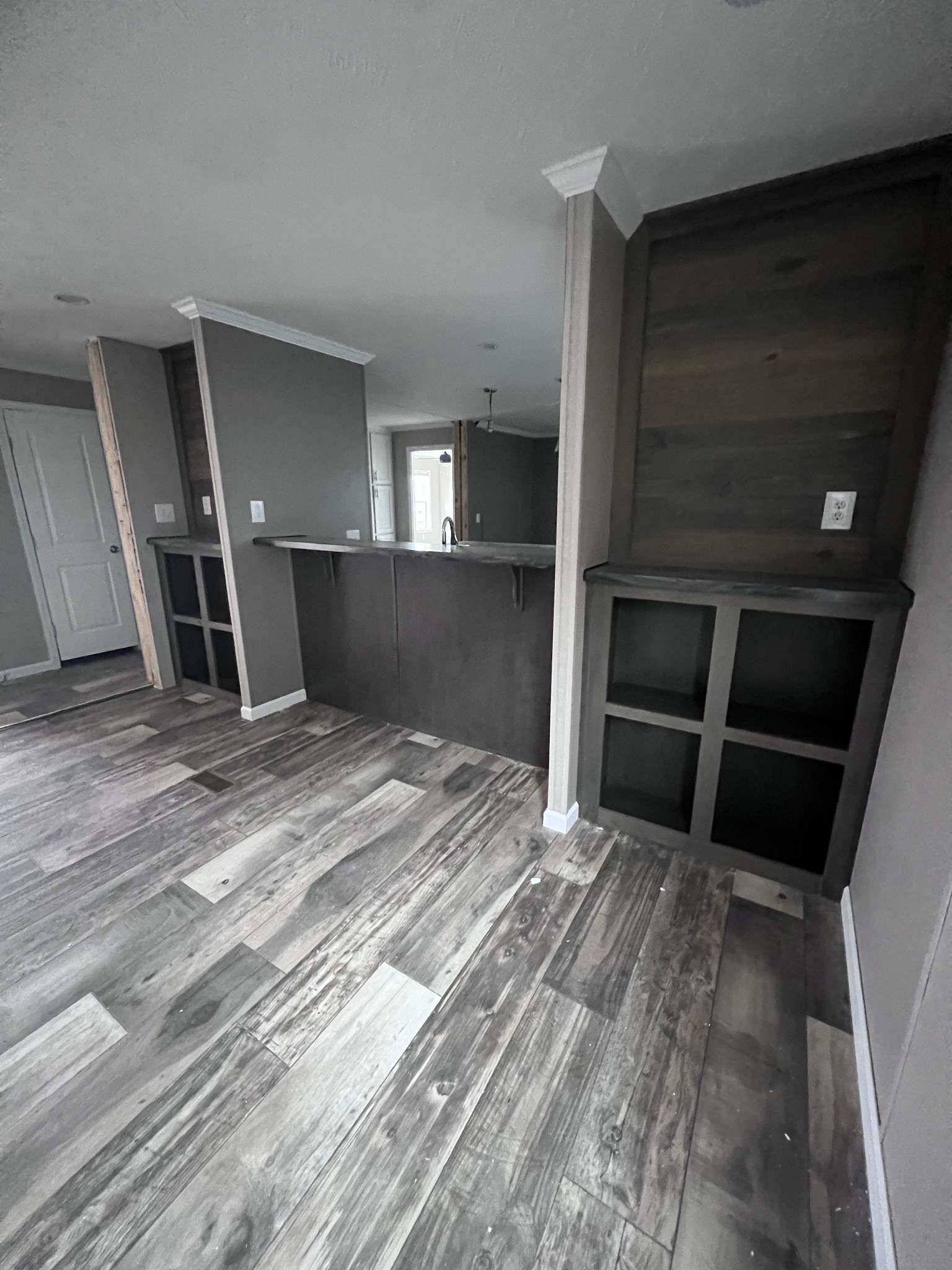 Open-concept room with gray walls and rustic wood flooring. Features inset shelves, a bar counter, pendant light, and white-paneled door, creating a modern feel.