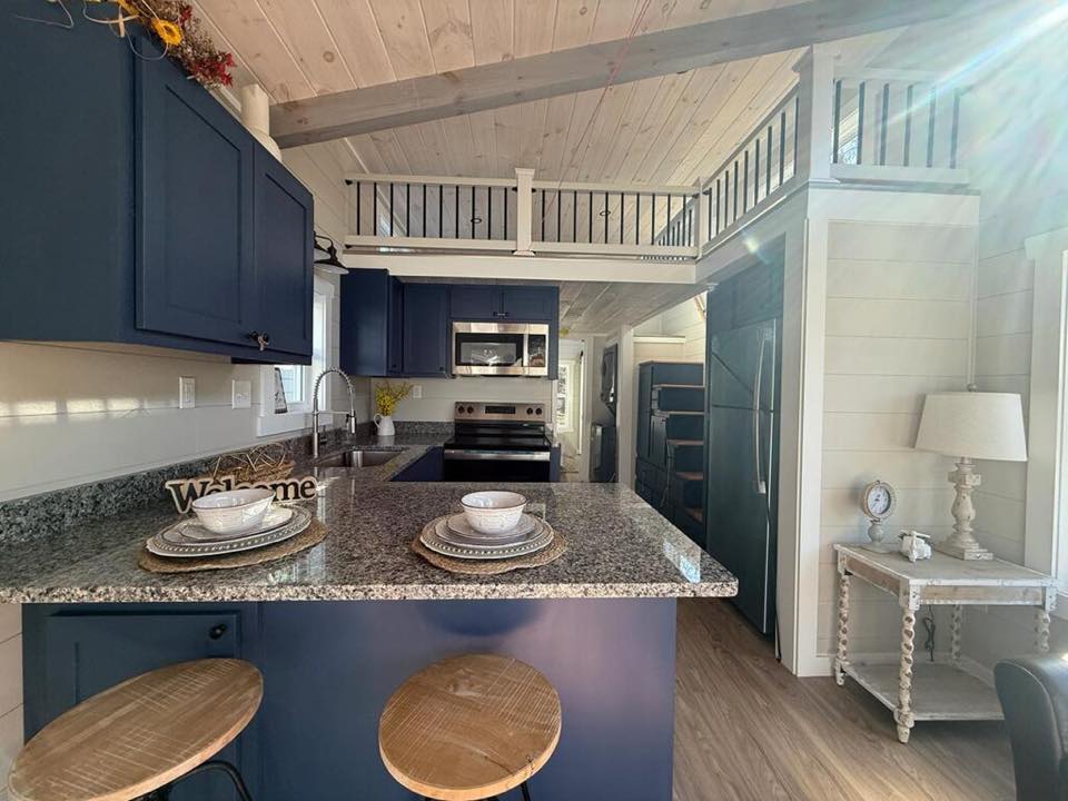 Cozy kitchen interior with navy cabinets, granite countertops, and bar stools. Warm lighting highlights a welcoming, rustic vibe.