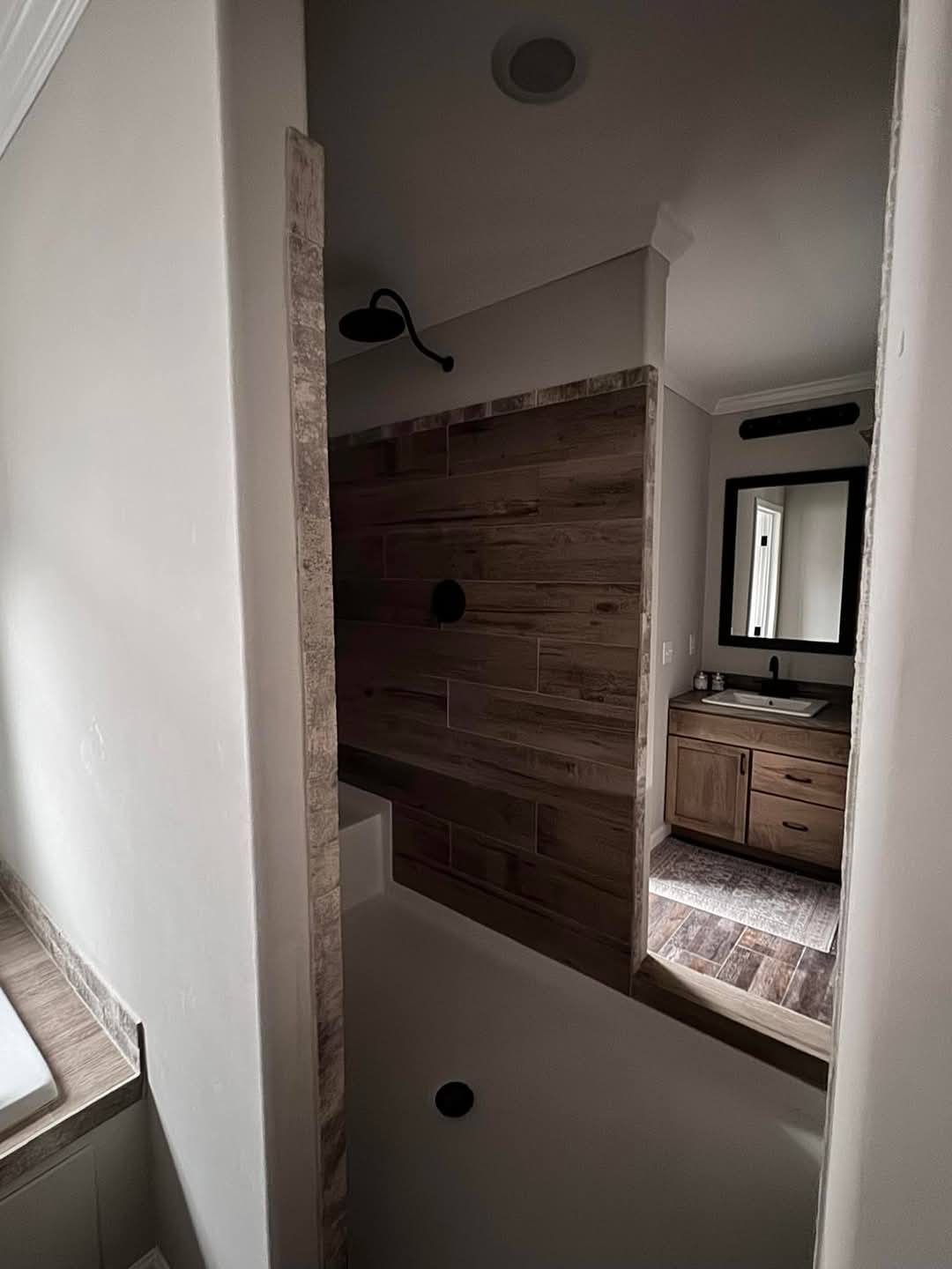 A cozy bathroom features a rustic wood-paneled shower, black fixtures, and a wooden vanity with a mirror. Soft, diffused lighting creates a warm ambiance.