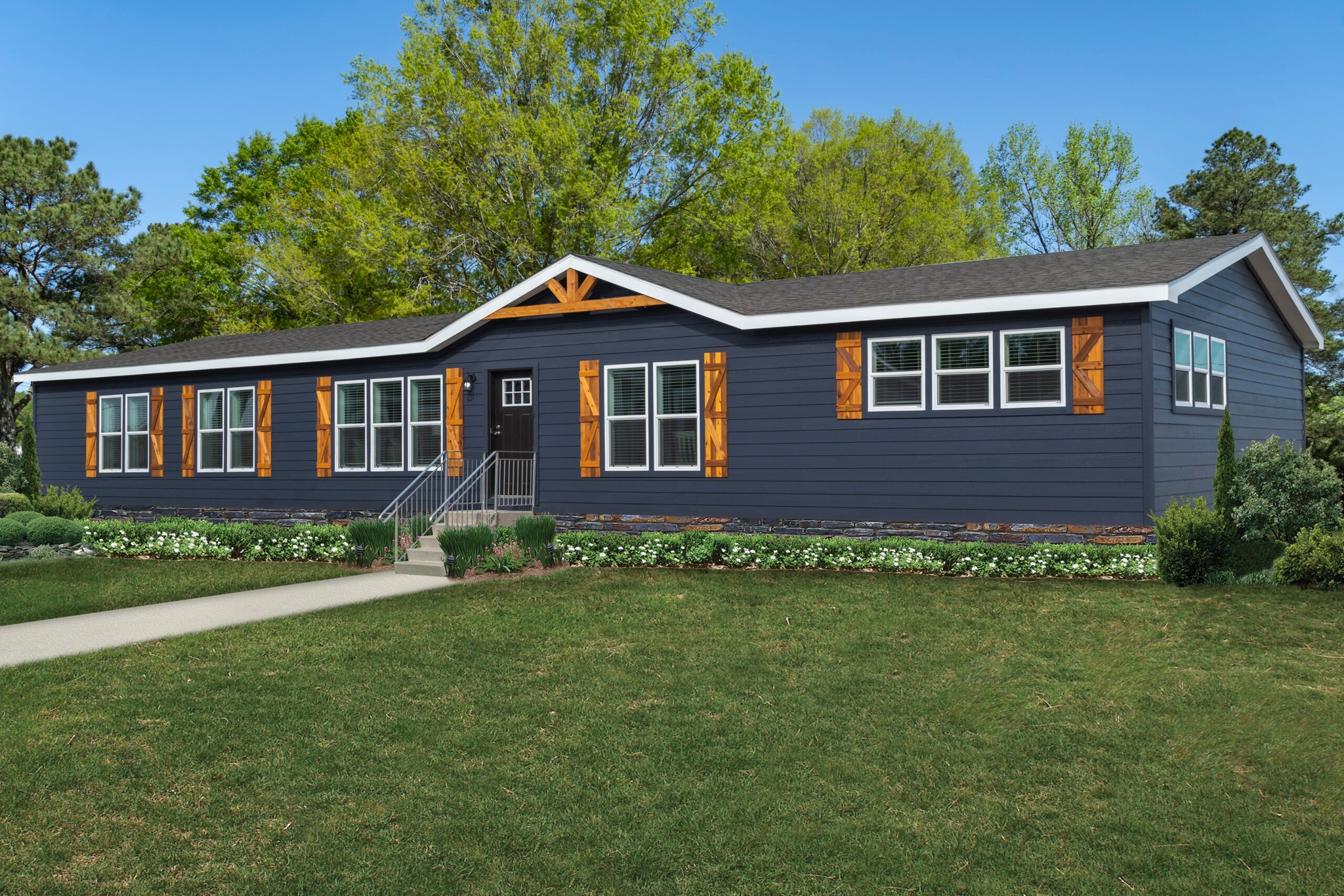 Single-story blue house with white trim and wooden shutters, surrounded by lush green lawn and trees. Bright, sunny day conveys a welcoming atmosphere.