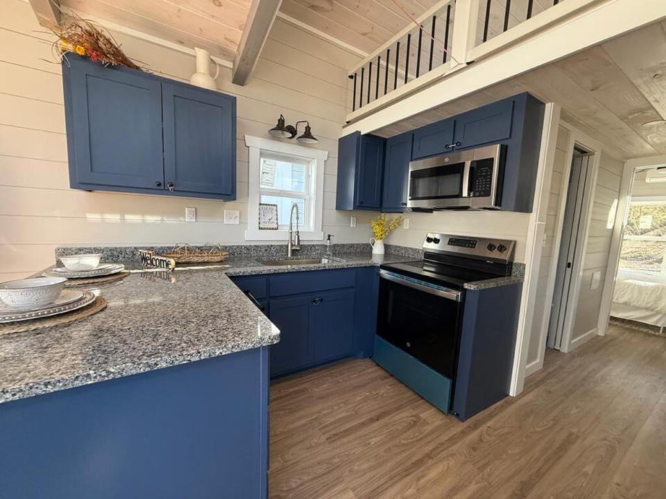 Cozy kitchen with blue cabinets, gray granite countertops, stainless steel appliances, and wooden floors. A vase with yellow flowers adds warmth.
