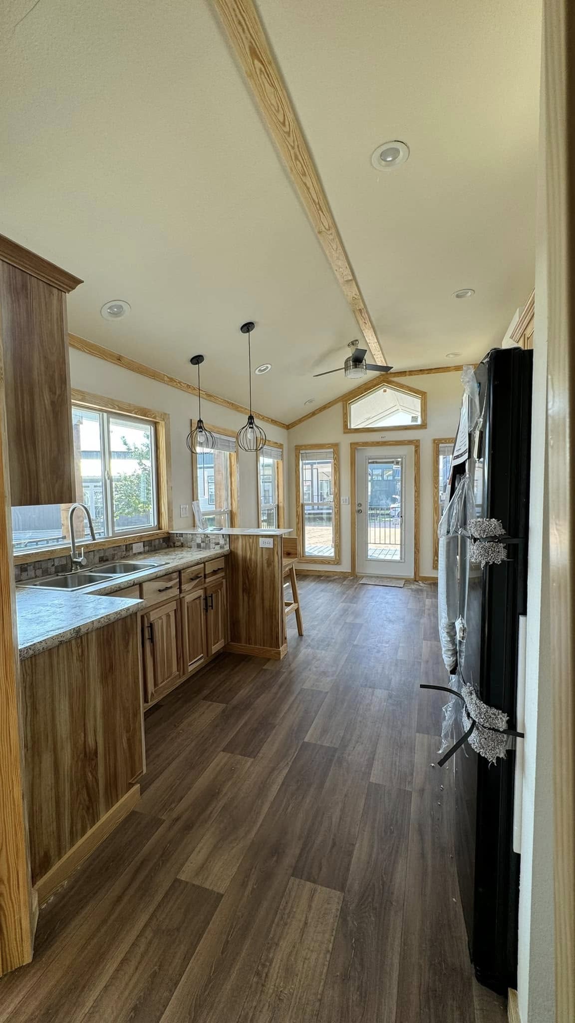 Bright kitchen with wood flooring, natural wood cabinets, and granite countertops. Two pendant lights hang over the island. Sunlit, welcoming atmosphere.