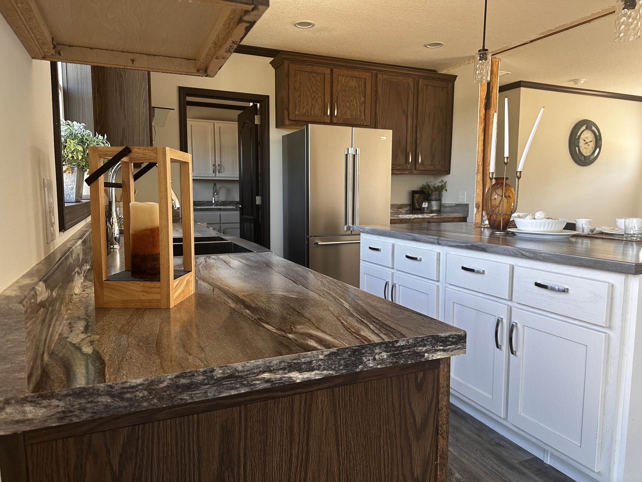 Modern kitchen with marble countertops, wooden cabinets, and stainless steel fridge. Candleholder and dishes add cozy and elegant touches. Warm lighting.