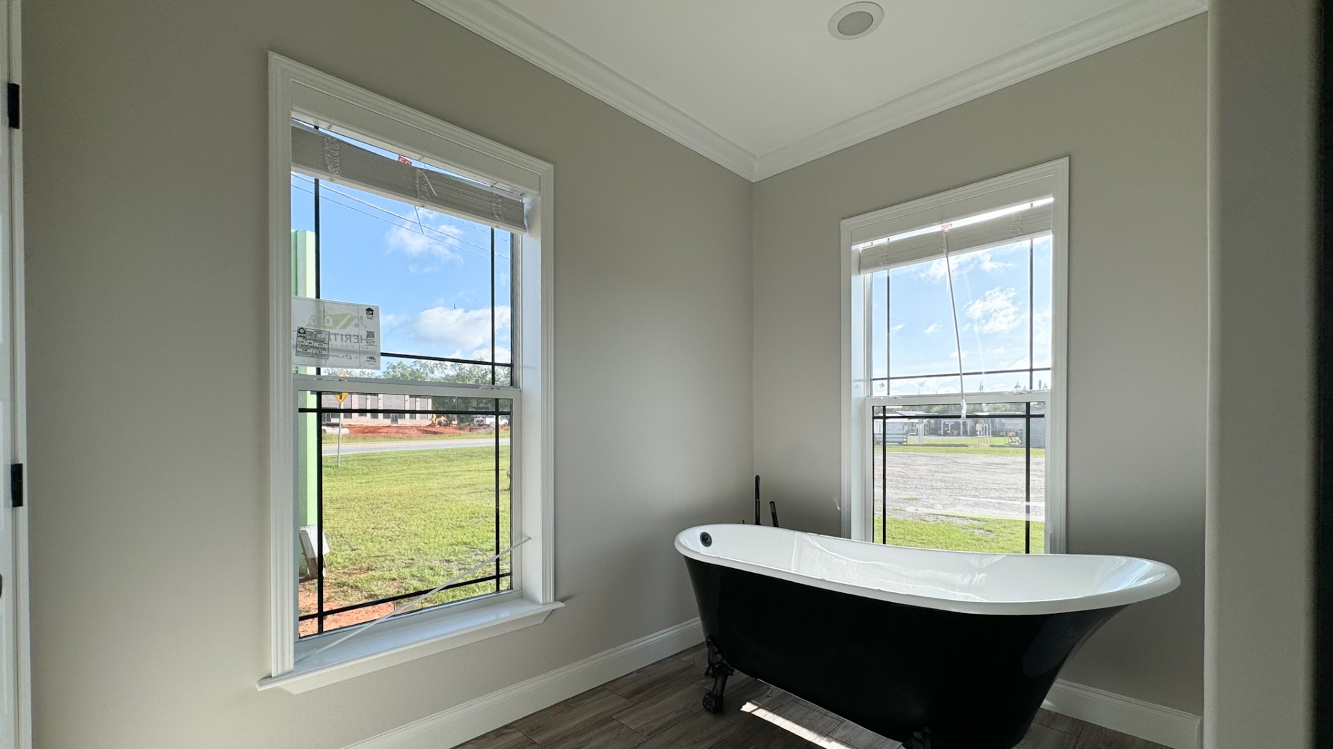 A serene bathroom with a vintage black and white clawfoot tub beneath two large windows. Soft natural light reflects on the light gray walls.