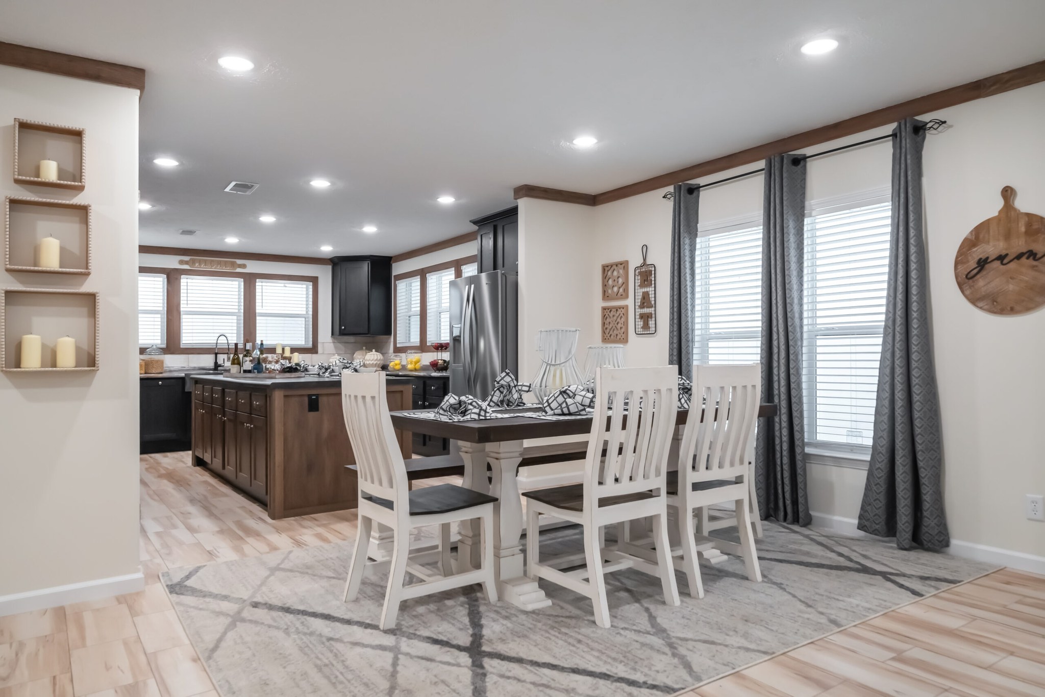 Modern kitchen and dining area with wooden floors and white walls. Features a table with white chairs, a central island, and large windows. Bright and welcoming.