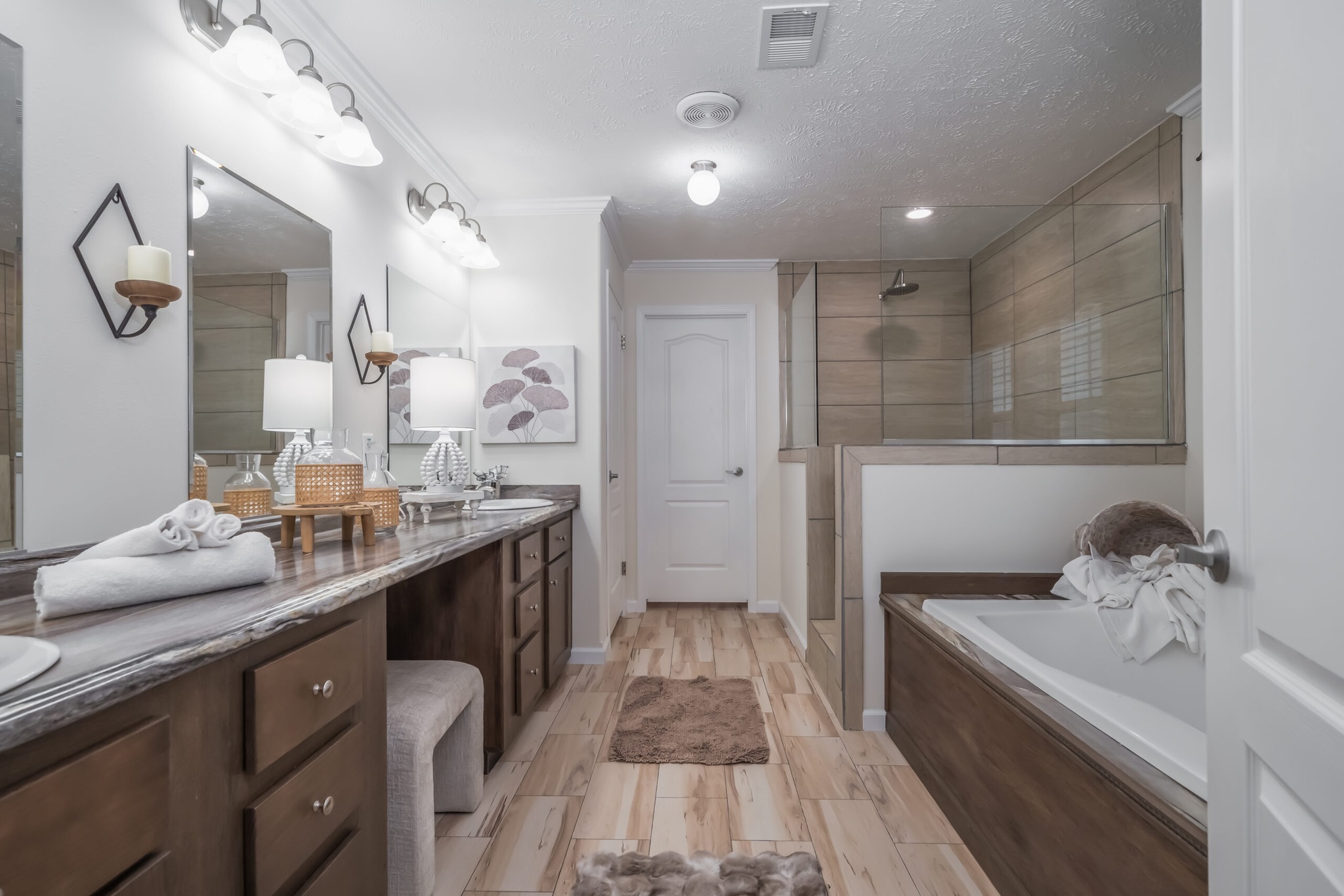 Spacious bathroom with dual sinks, large mirrors, and wood accents. A glass-enclosed shower and a tub are visible, creating a serene, modern feel.
