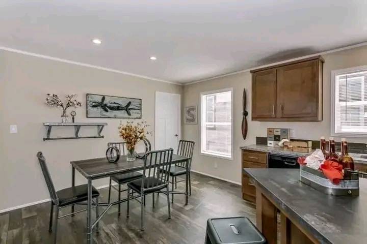 Cozy kitchen with wooden cabinets and dark countertop. A metal dining set with floral centerpiece sits on a wooden floor. Walls feature nature-themed decor.