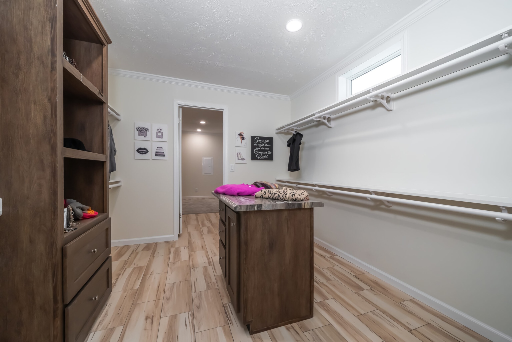 Spacious walk-in closet with wood shelves and drawers on the left, white walls, and hanging rods. Center island with folded clothes. Bright and organized.