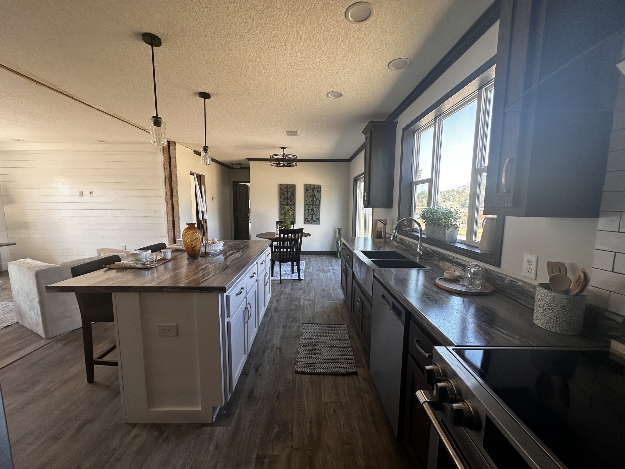 Bright kitchen with dark wood countertops and white cabinetry, featuring a large island. Pendant lights hang above, leading to a cozy dining area.