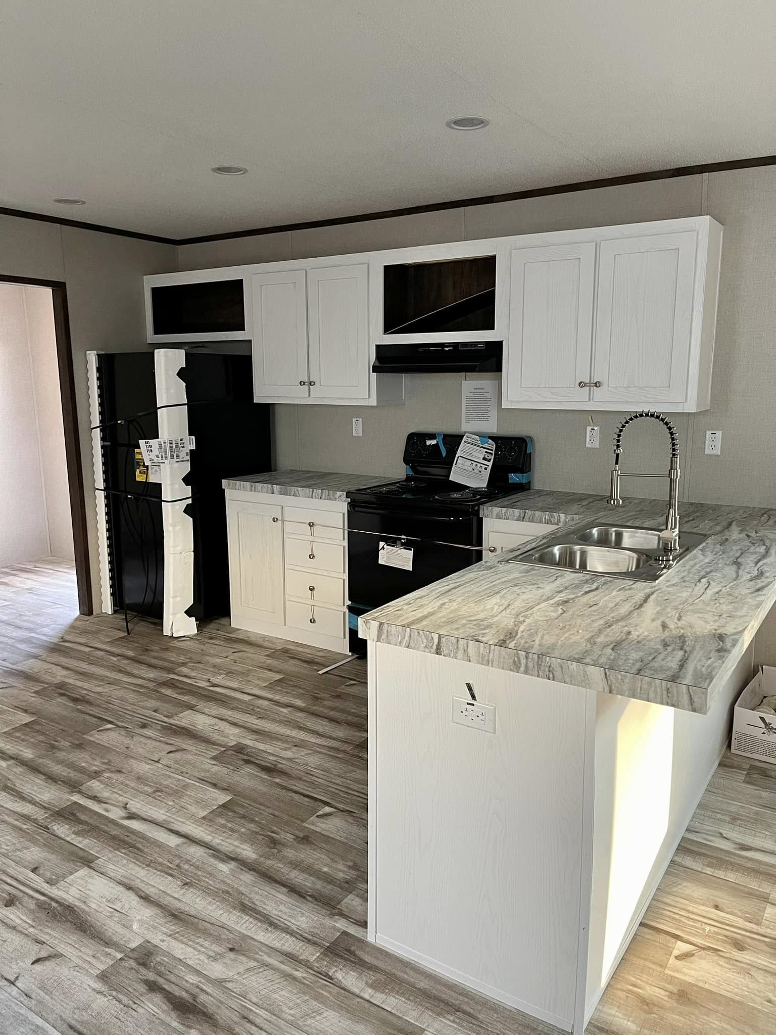 Modern kitchen with white cabinets and marble countertops. Features a stainless steel sink, black appliances, and light wood flooring, creating a fresh, inviting atmosphere.