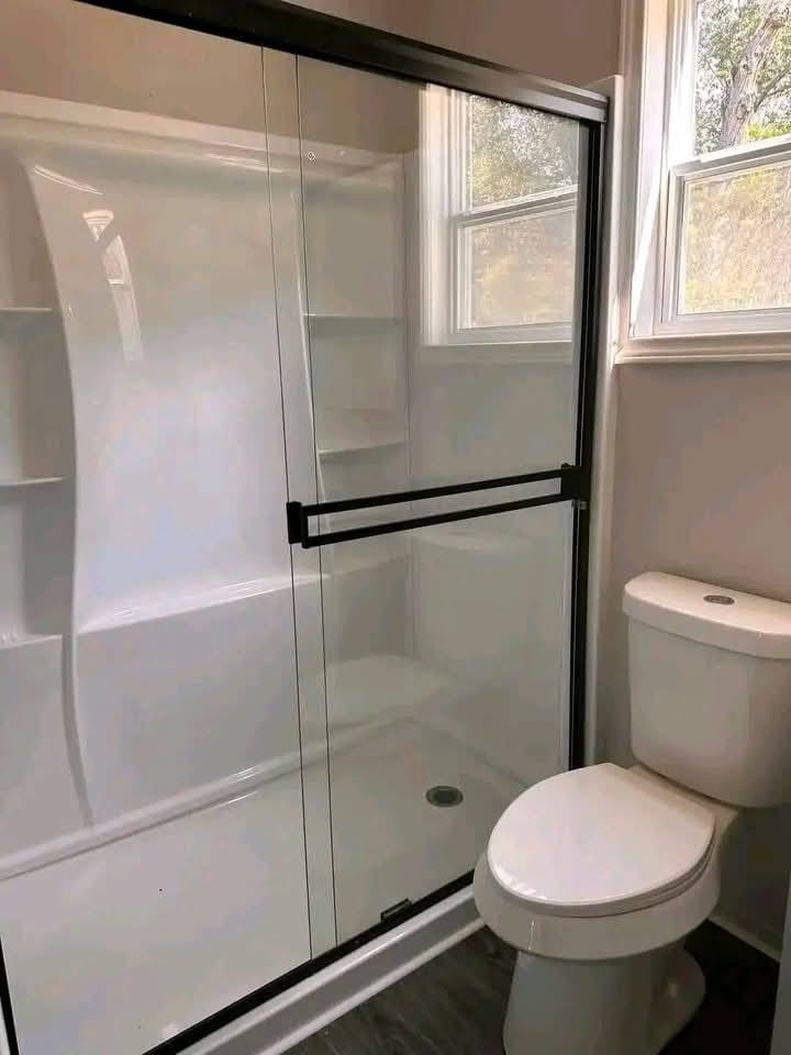 Modern bathroom with a white toilet and a sleek glass-enclosed shower. The room feels bright and clean, with soft natural light from a window.