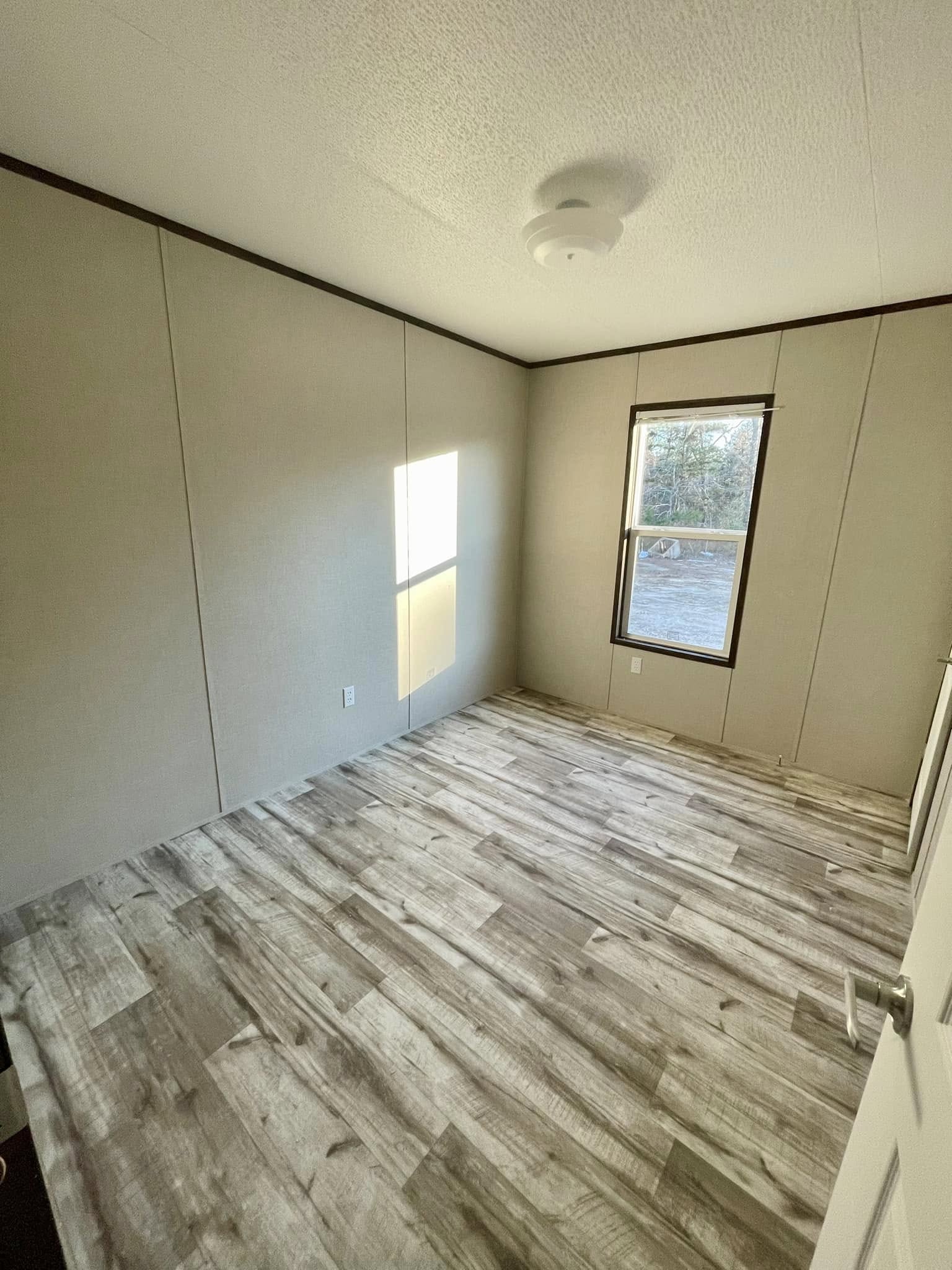 Empty room with light beige walls and a window letting in natural light. Wooden floor with a grayish tone. The atmosphere is calm and minimalist.