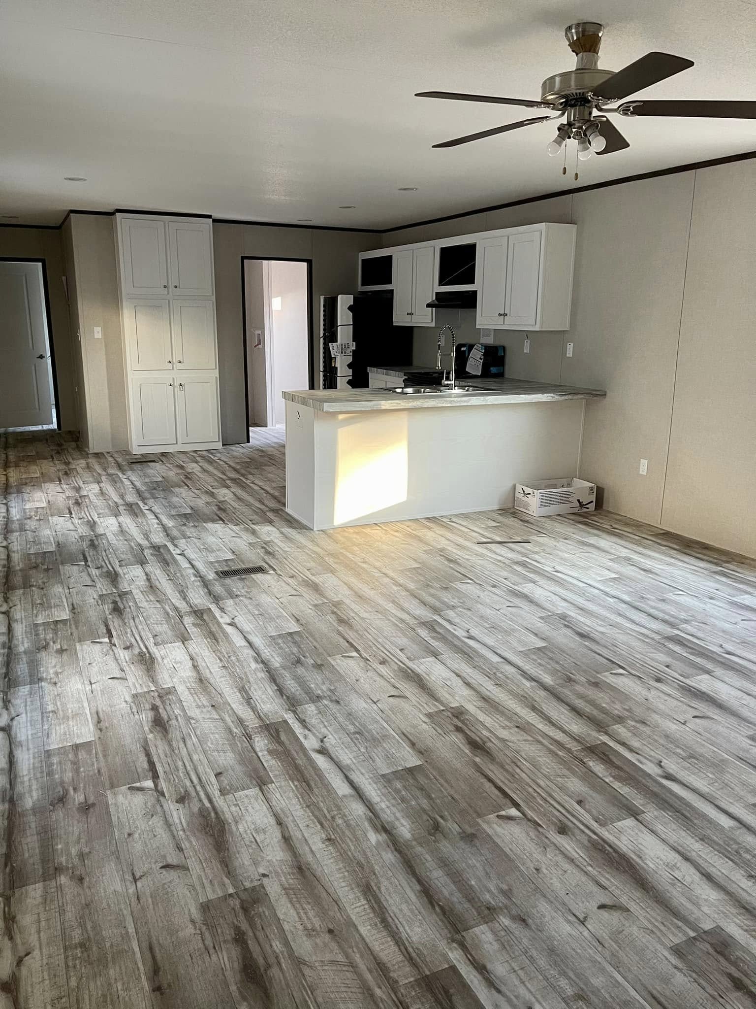 Spacious modern kitchen with light wood flooring and white cabinets. A ceiling fan hangs above, and sunlight streams in, creating a warm ambiance.