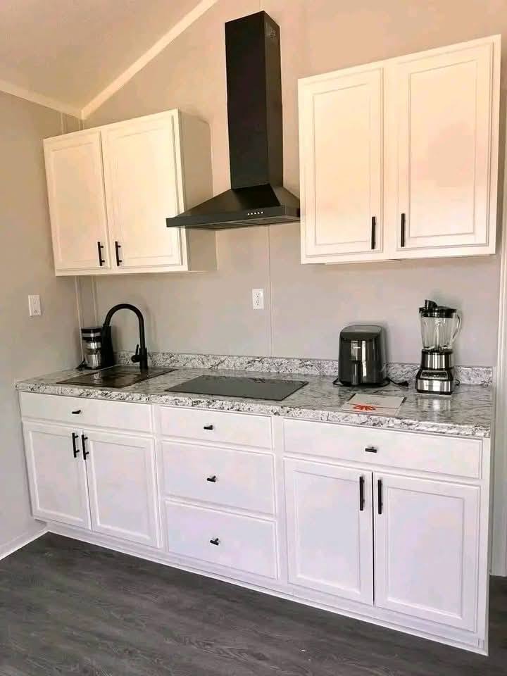 Modern kitchen with white cabinets, marble countertop, and black appliances. Includes a blender, coffee maker, gas cooktop, black faucet, and range hood.