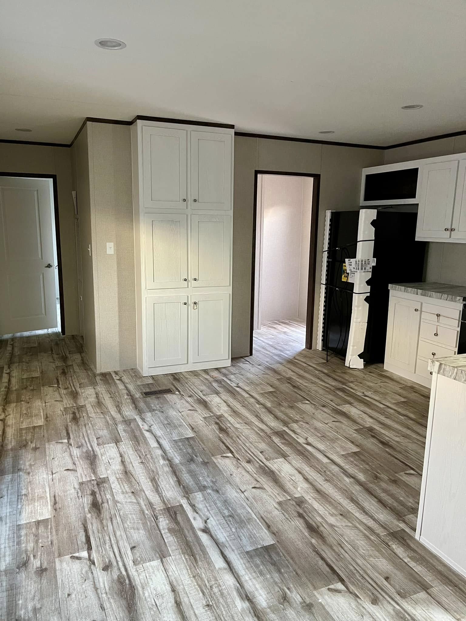 Spacious kitchen with rustic wood flooring, white cabinets, and black appliances. Bright with natural light, offering a cozy and modern feel.