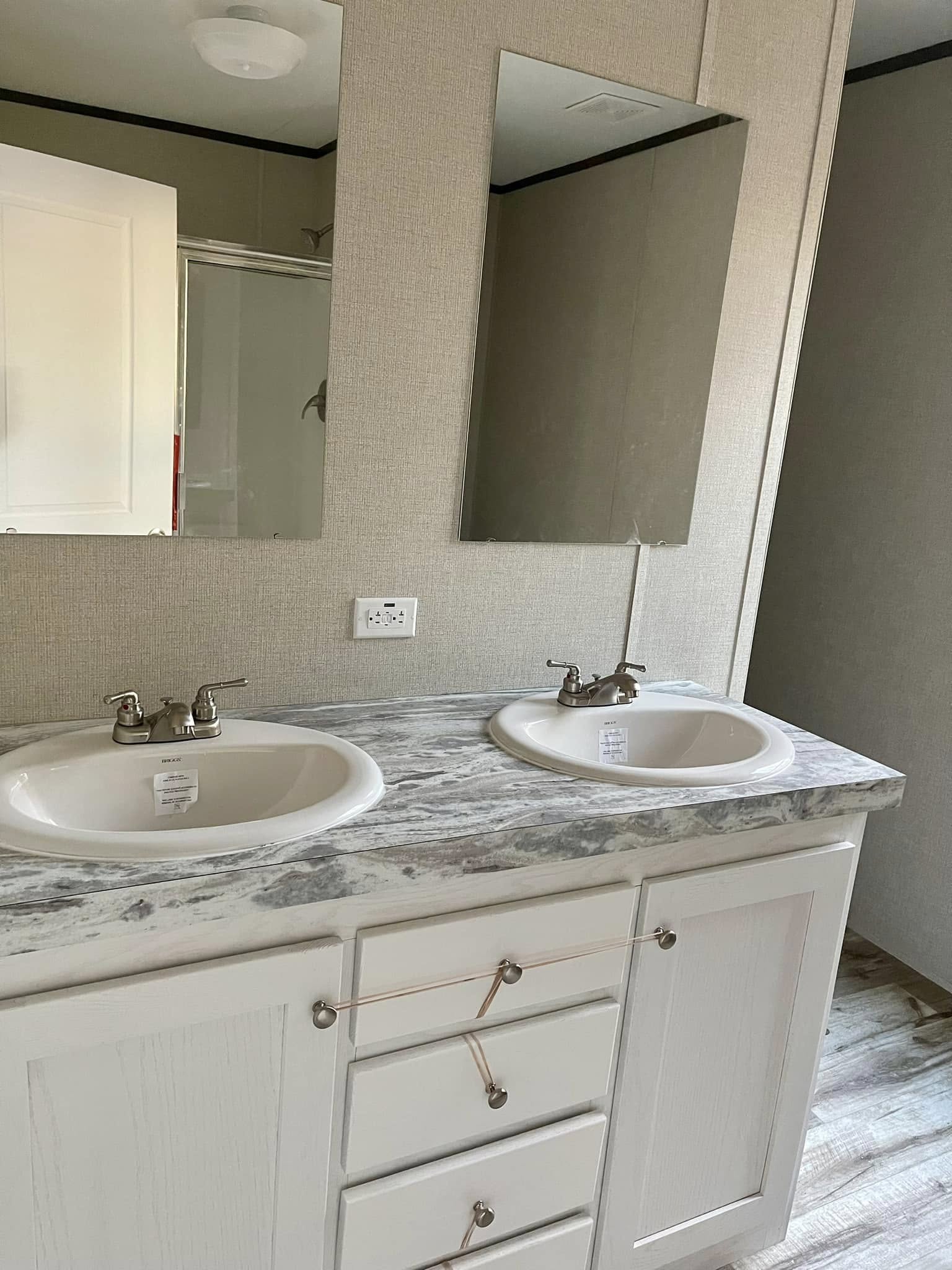 Dual sinks with silver faucets sit on a marble countertop in a bathroom. Two mirrors are above the sinks, and white cabinets with rope ties are below.