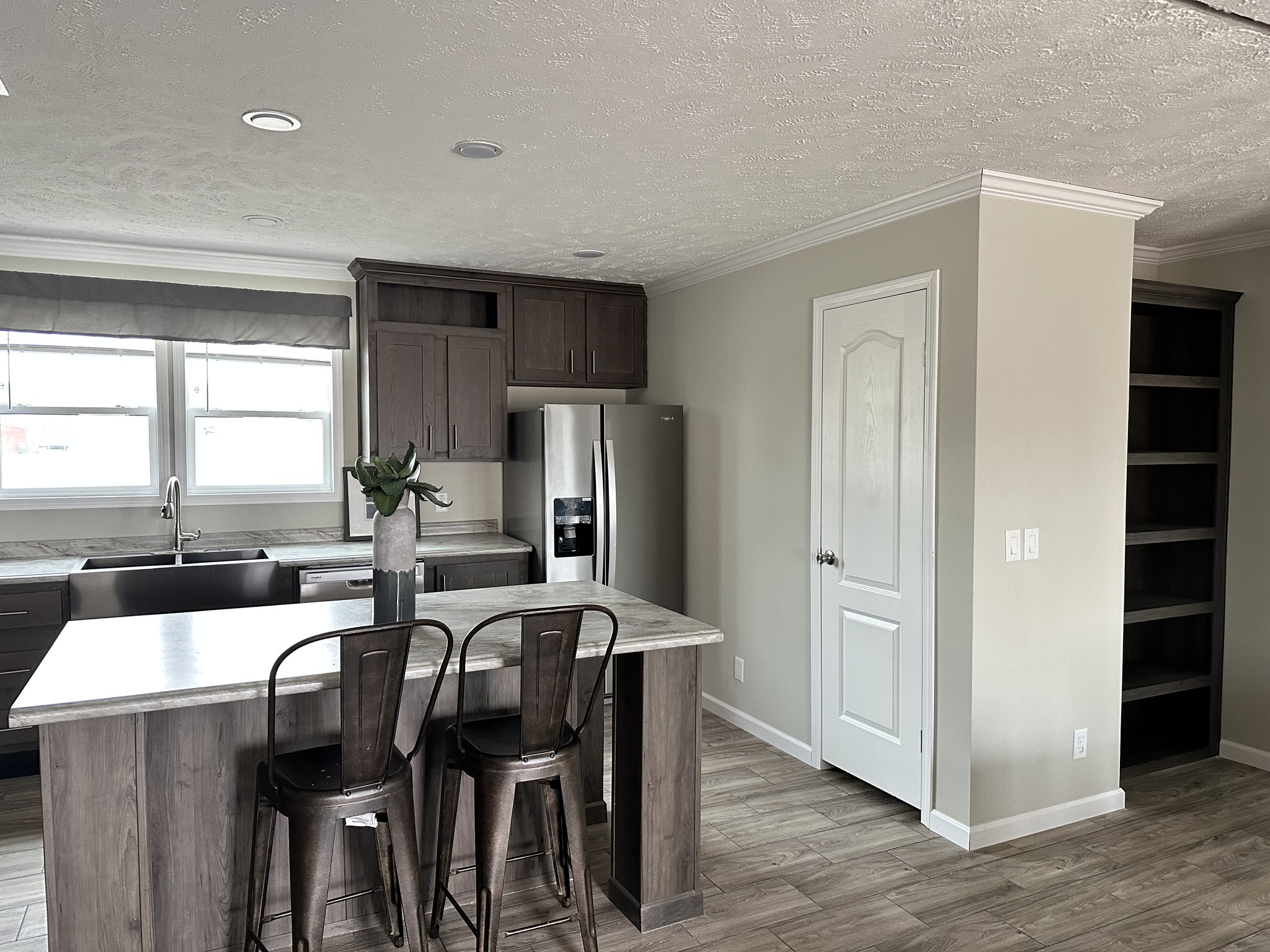 Modern kitchen with wooden cabinets, stainless steel appliances, and a center island with two metal chairs. A vase with flowers adds a touch of elegance.