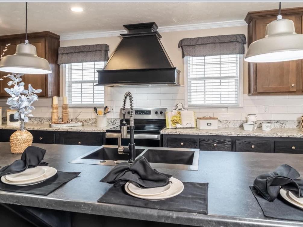 Spacious kitchen with dark countertops, modern black fixtures, and a central island set for three with black napkins. Bright ambiance with elegant decor.