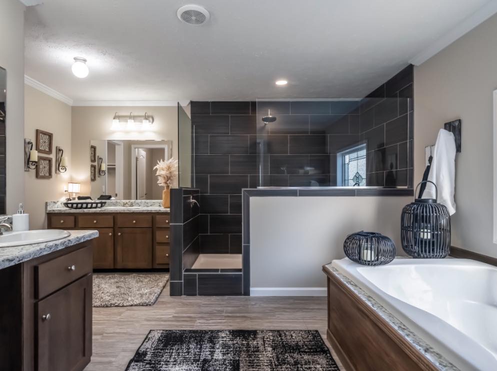 Spacious bathroom with a modern aesthetic, featuring a large bathtub, sleek dark tile shower, wooden cabinets, and elegant lighting fixtures.