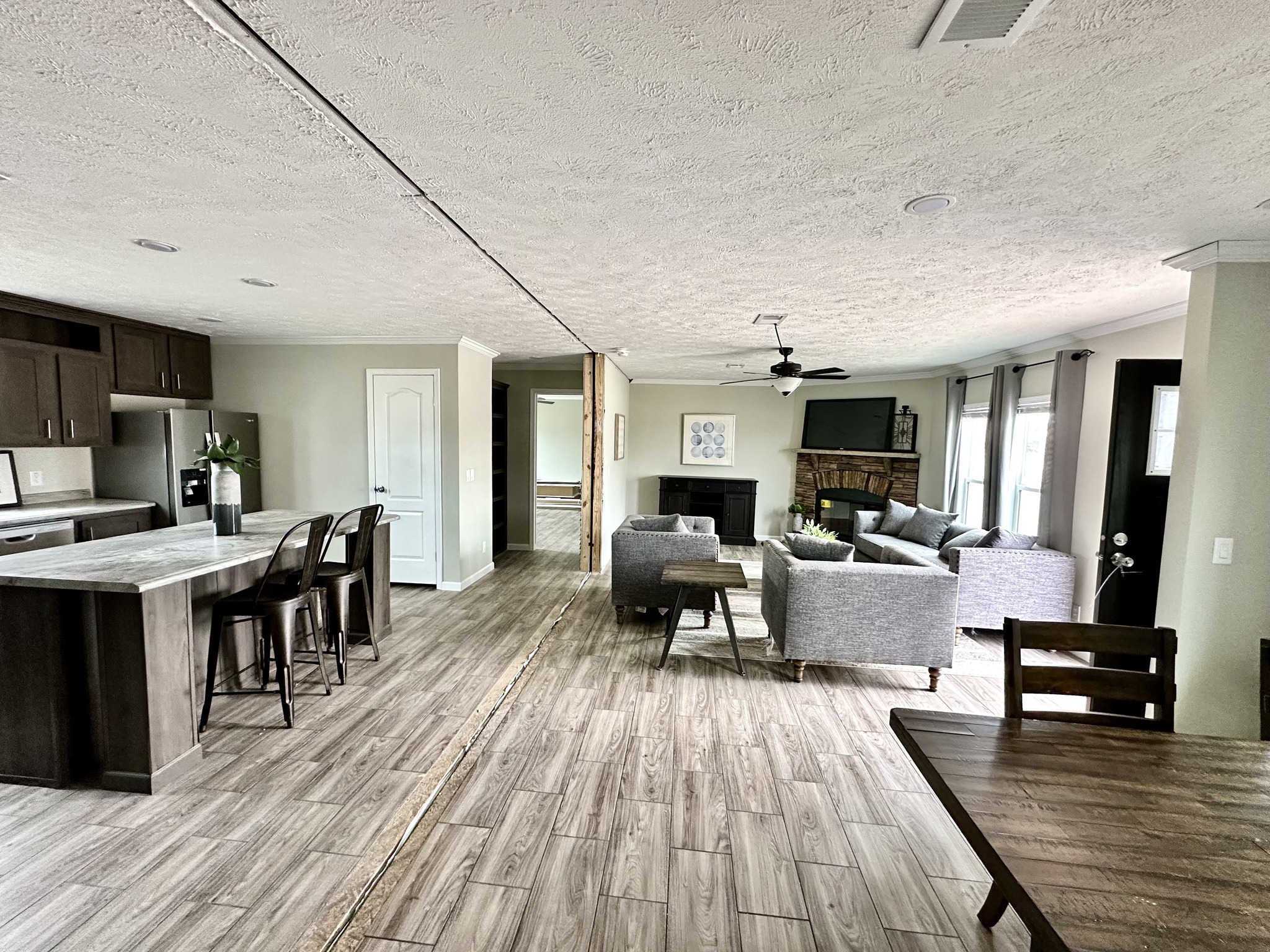 Spacious modern living area with open-plan kitchen and seating. Features wood flooring, neutral tones, and large windows offering natural light.