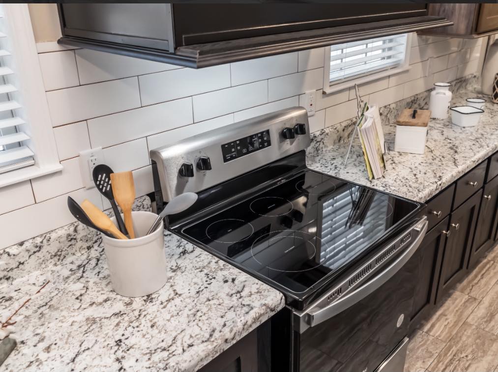Modern kitchen with white tile backsplash, granite countertops, and a sleek black electric stove. Utensils in a holder convey a tidy ambiance.