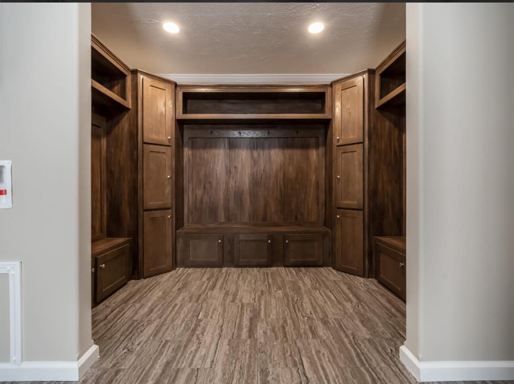 Long, wooden built-in mudroom storage with high cabinets, open shelving, and hooks on a paneled backdrop. The tone is warm and organized.