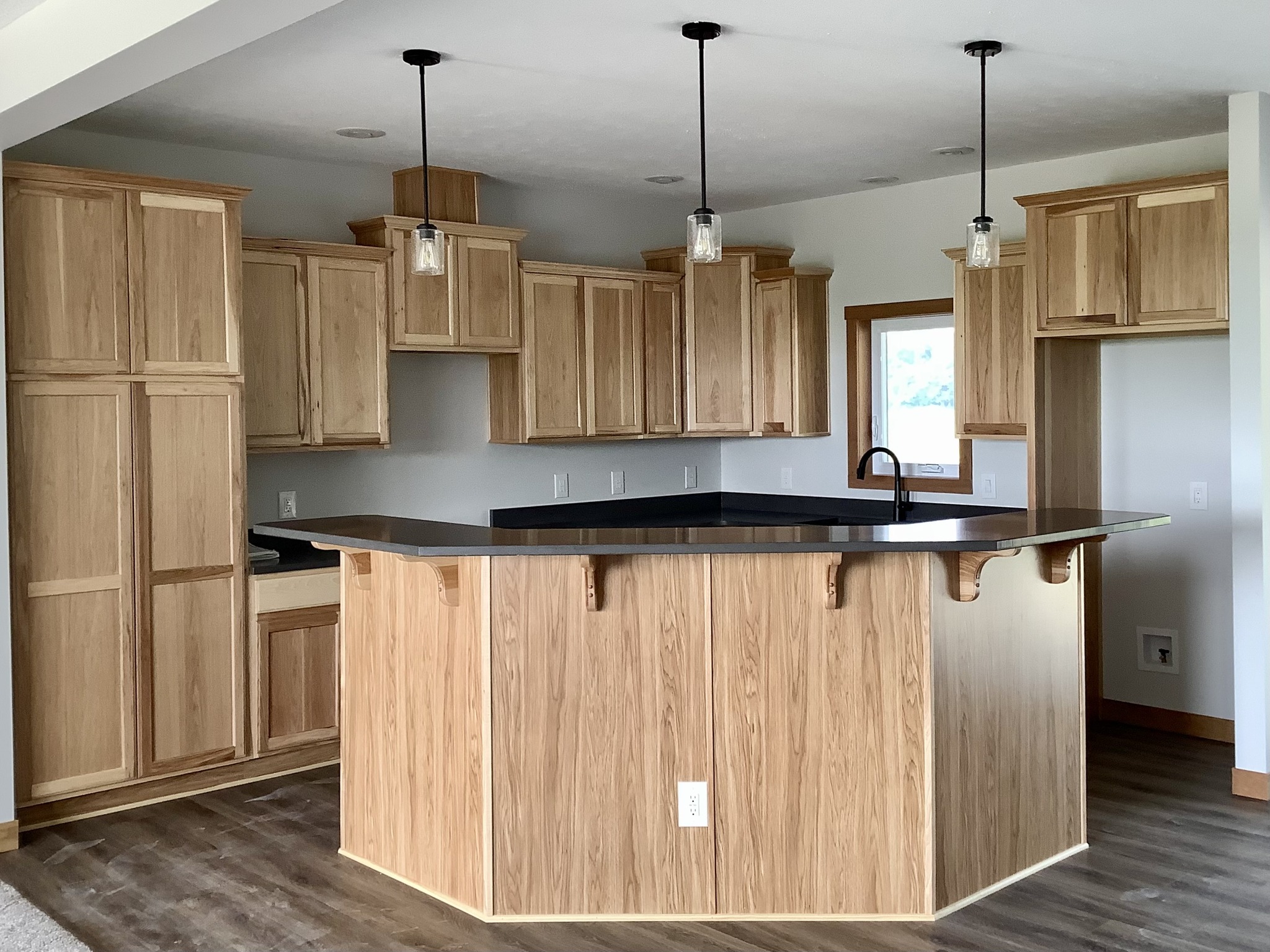 Spacious kitchen with light wood cabinets and a large island countertop. Three pendant lights hang from the ceiling, creating a warm, inviting atmosphere.