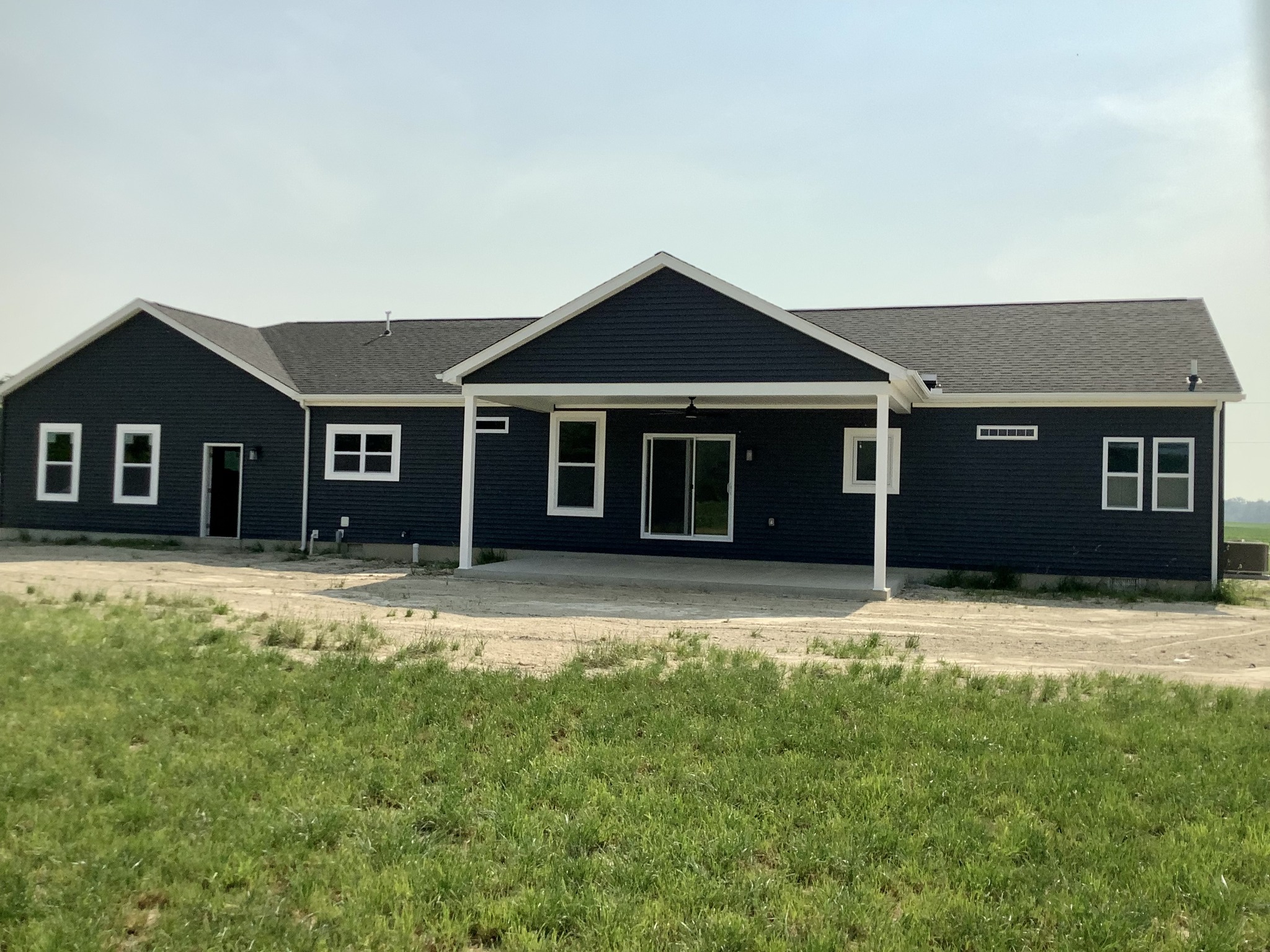 Single-story navy blue house with white trim, large windows, and a covered porch. Set amidst a grassy yard under a clear, bright sky.