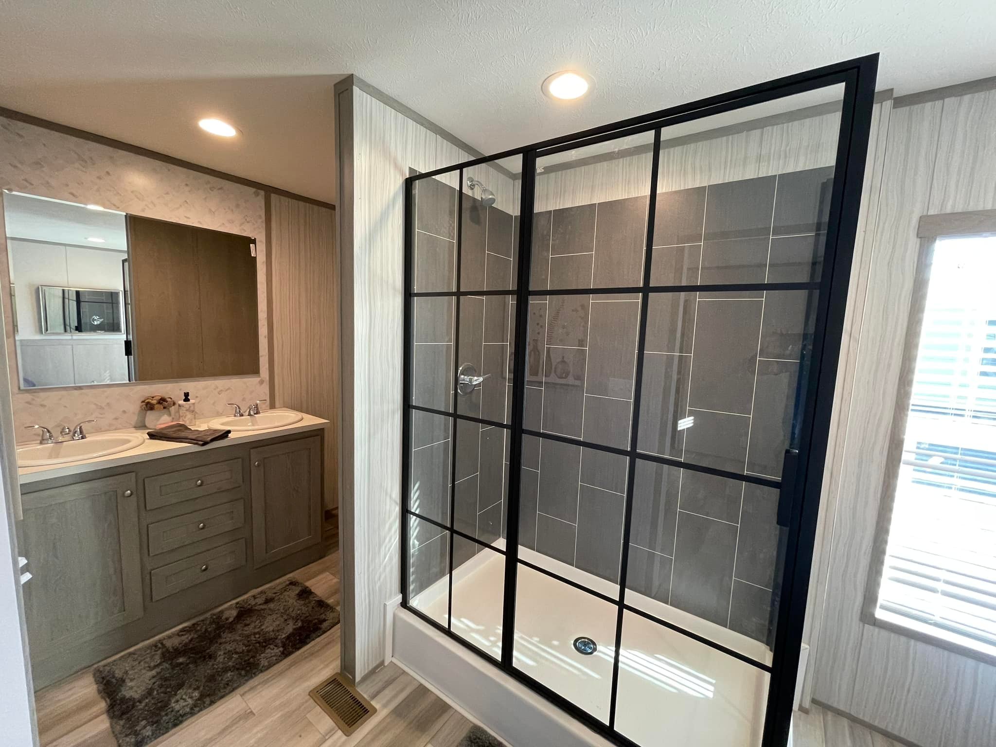 Modern bathroom with a spacious glass shower featuring dark tiles and a sleek black frame. Double sink vanity with large mirror and soft lighting.
