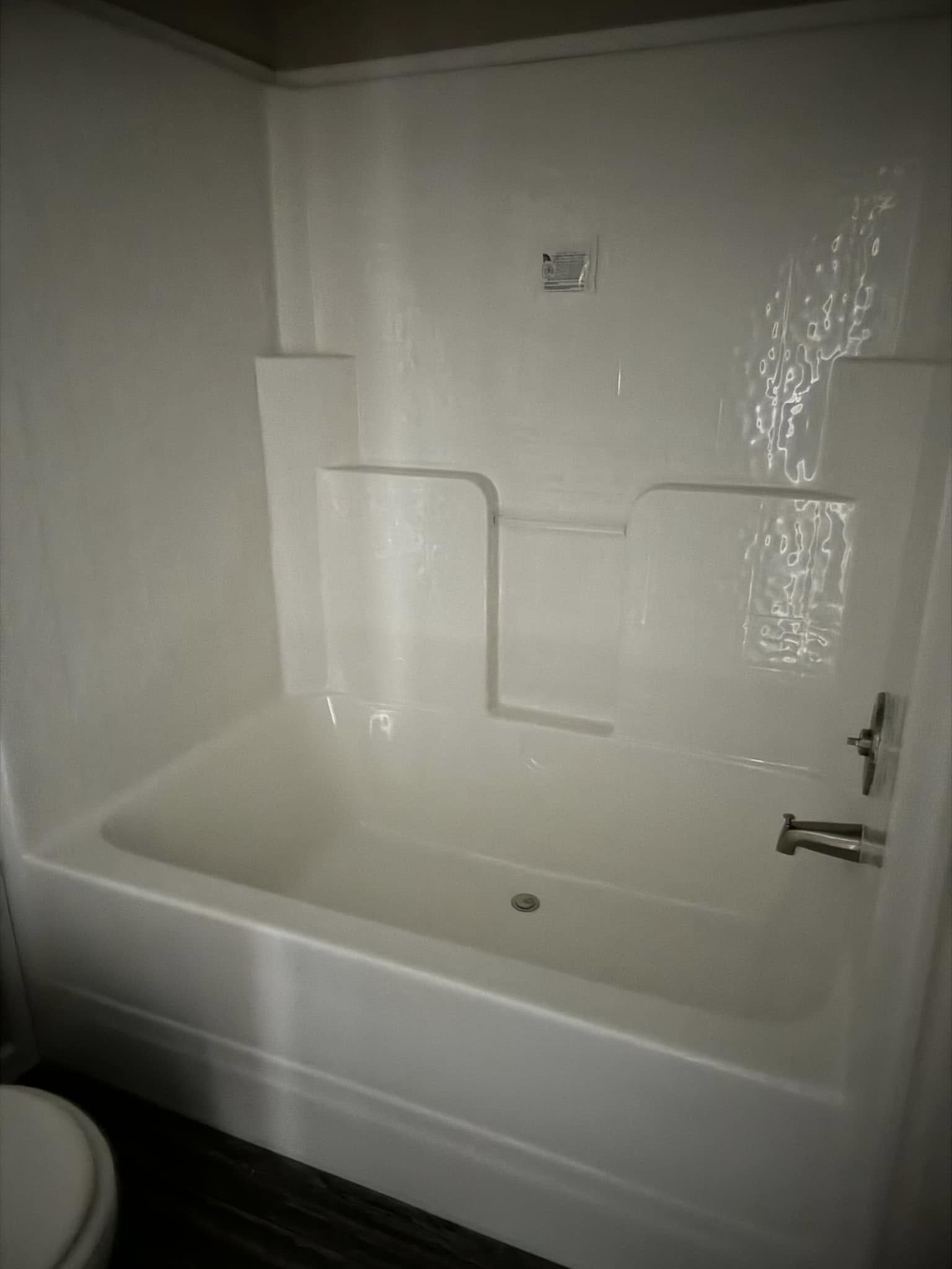 White bathtub and shower combo with built-in shelving against a smooth wall. Chrome faucet and textured floor enhance a clean, modern look.
