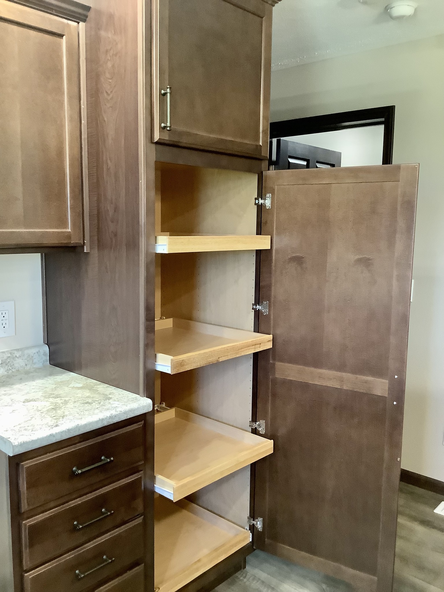Wooden kitchen cabinet with open pull-out pantry shelves next to a countertop. The room has a modern, organized feel with ample storage.