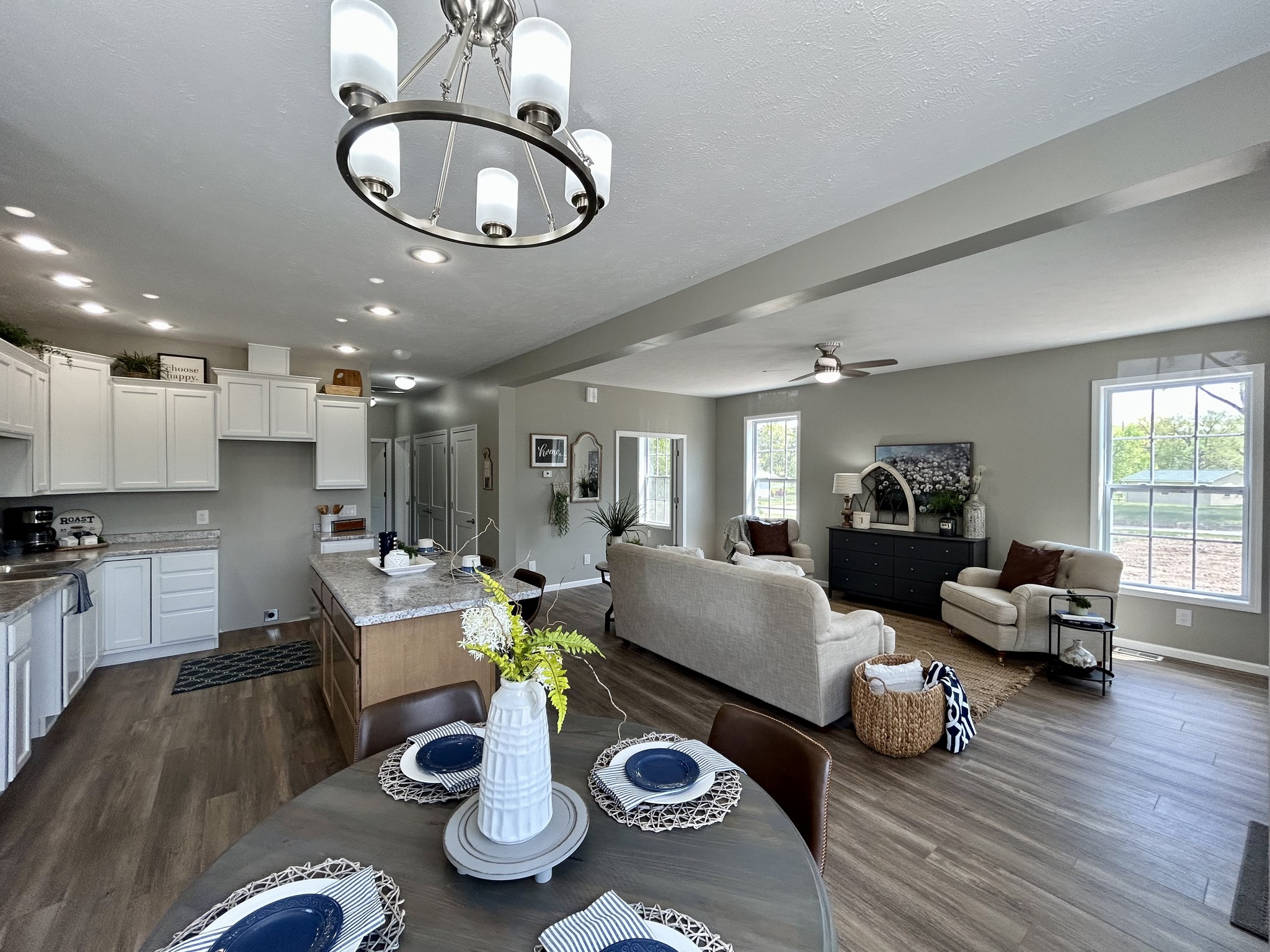 Modern, open-concept living room and kitchen with neutral tones. Features a dining table set for four, cozy seating, and bright natural light.