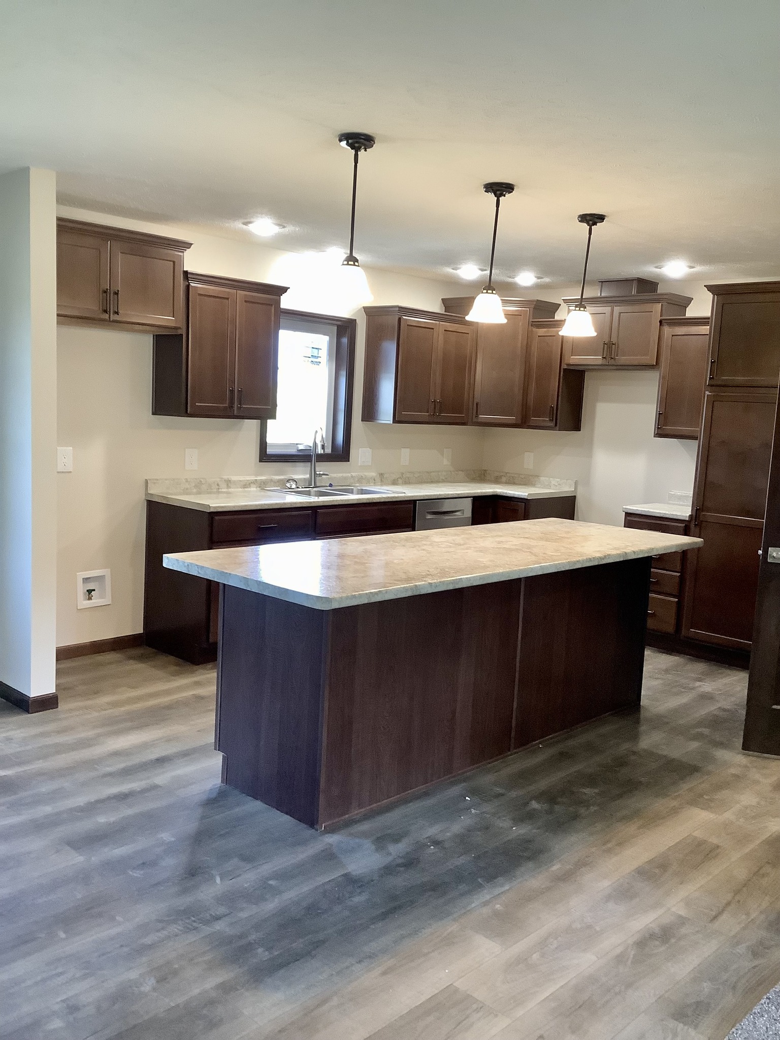 Modern kitchen with dark wood cabinets, a central island with light countertops, stainless steel appliances, and three pendant lights, creating a warm ambiance.