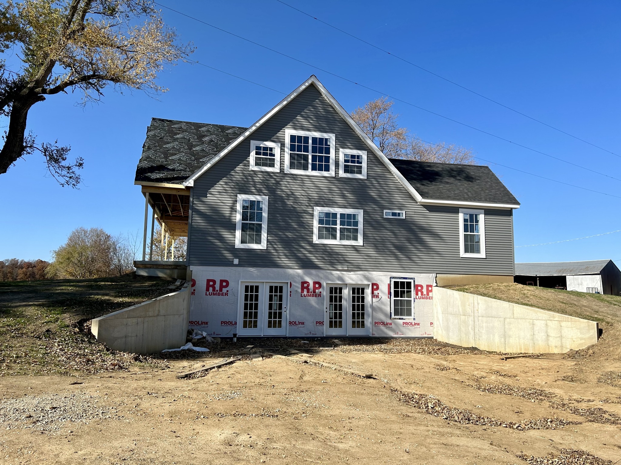 A gray house under construction with multiple windows and a steeply pitched roof against a clear blue sky. The foundation is exposed, showing concrete walls.