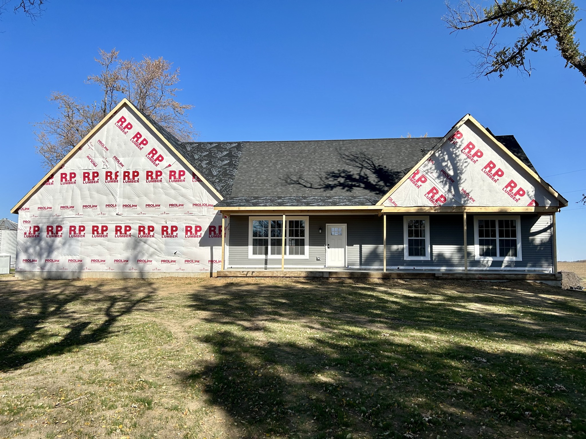 Newly constructed house under a clear blue sky, with gray siding and partial roofing. The left and right gables show exposed insulation with RP logos.