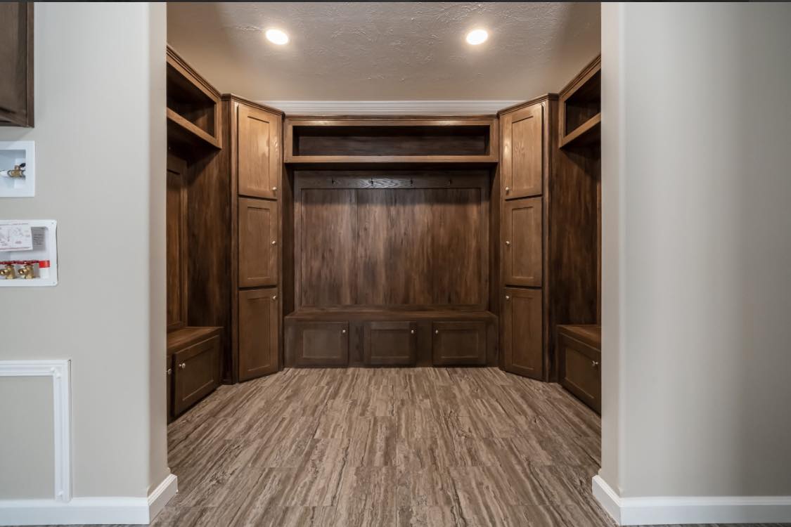 Spacious mudroom with dark wood built-in storage cabinets and bench, well-lit by recessed ceiling lights. The space feels warm and organized.