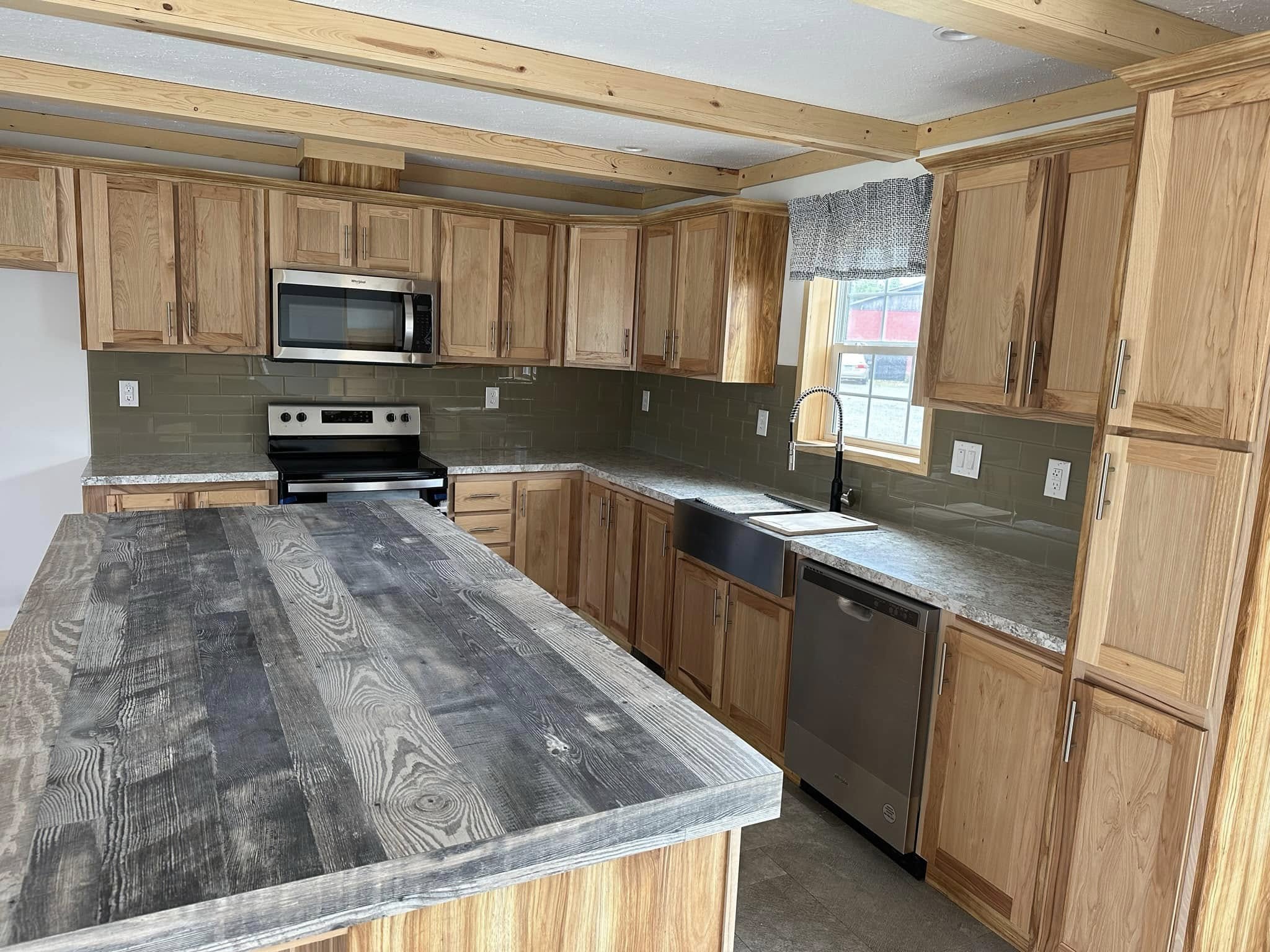 A modern kitchen with rustic charm, featuring wooden cabinets, a large wooden island, stainless steel appliances, and a farmhouse sink. Natural light brightens the space, creating a warm, inviting atmosphere.