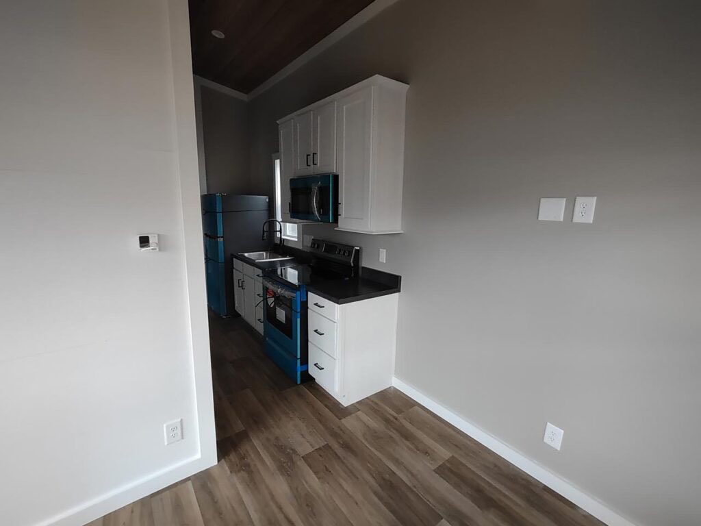 Compact kitchen with white cabinets, black countertops, and blue appliances. Wood flooring and gray walls create a modern, minimalist feel.