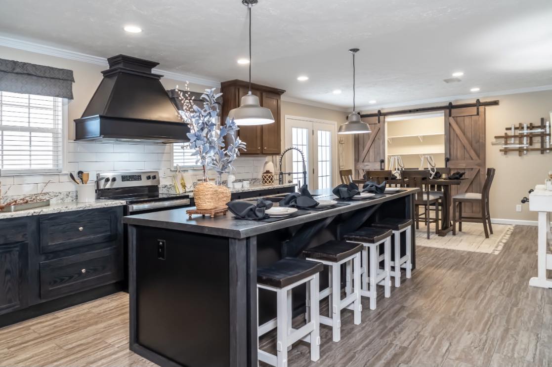 Spacious kitchen with dark cabinets, central island with bar stools, pendant lights, barn door, wood floor; elegant and inviting ambiance.