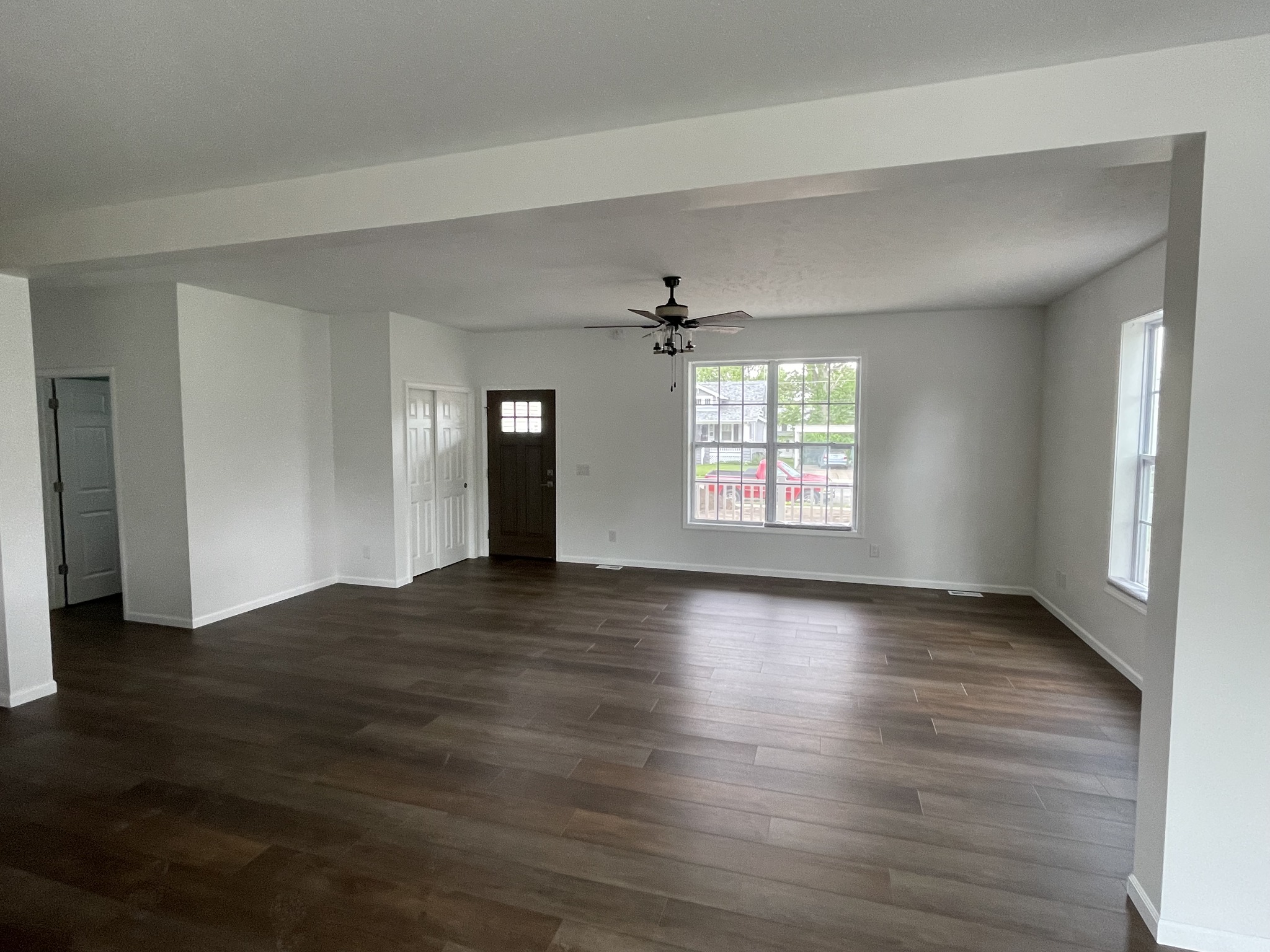 Spacious empty room with wooden flooring, white walls, large windows, and a ceiling fan. Natural light creates a bright, open, inviting atmosphere.