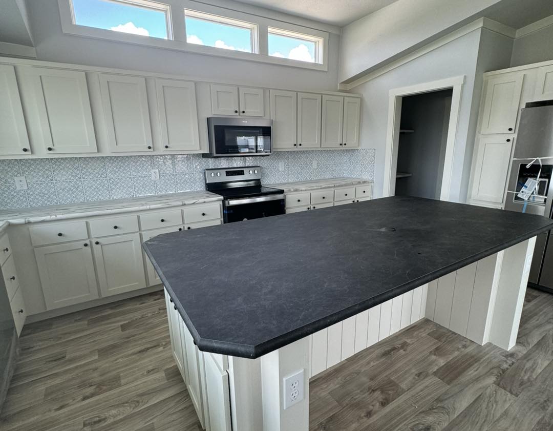 Spacious kitchen with a large dark countertop island, white cabinets, stainless steel appliances, and light wood flooring. Bright and modern ambiance.