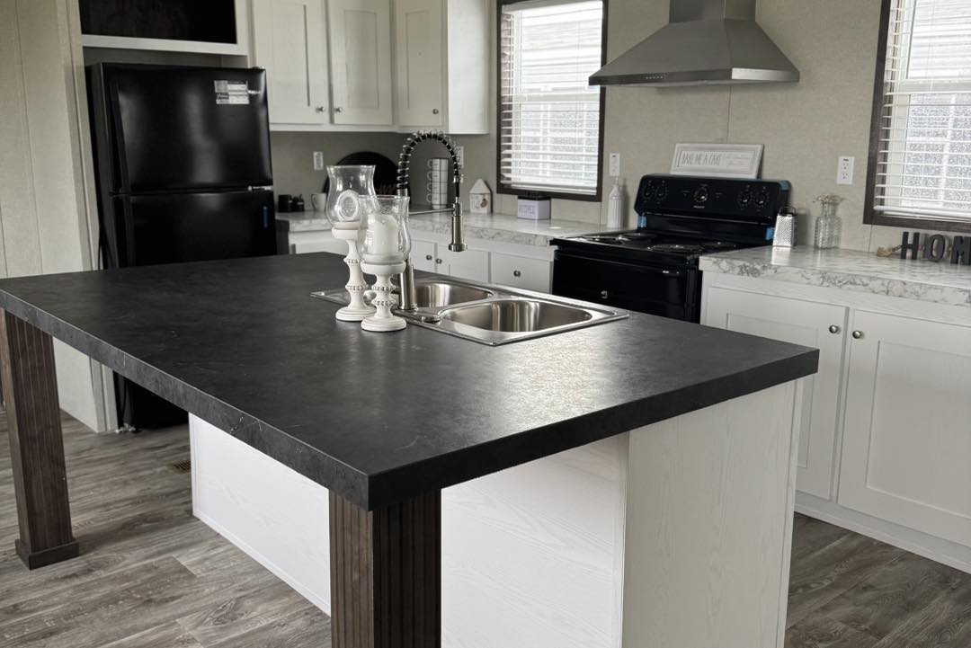 Modern kitchen with sleek black countertops, white cabinets, and stainless steel appliances. The central island features a double sink and decorative candles, exuding a clean, contemporary vibe.