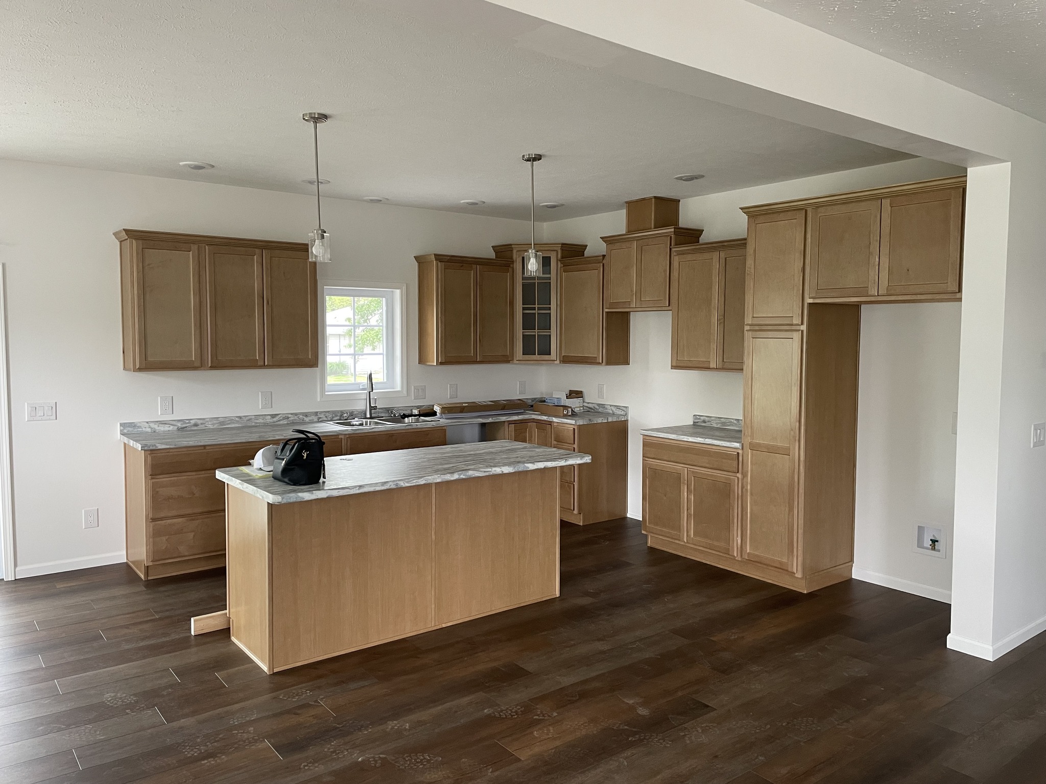 A modern kitchen with wooden cabinets, a marble countertop island, and pendant lights; bright, fresh, and open atmosphere with dark wood flooring.