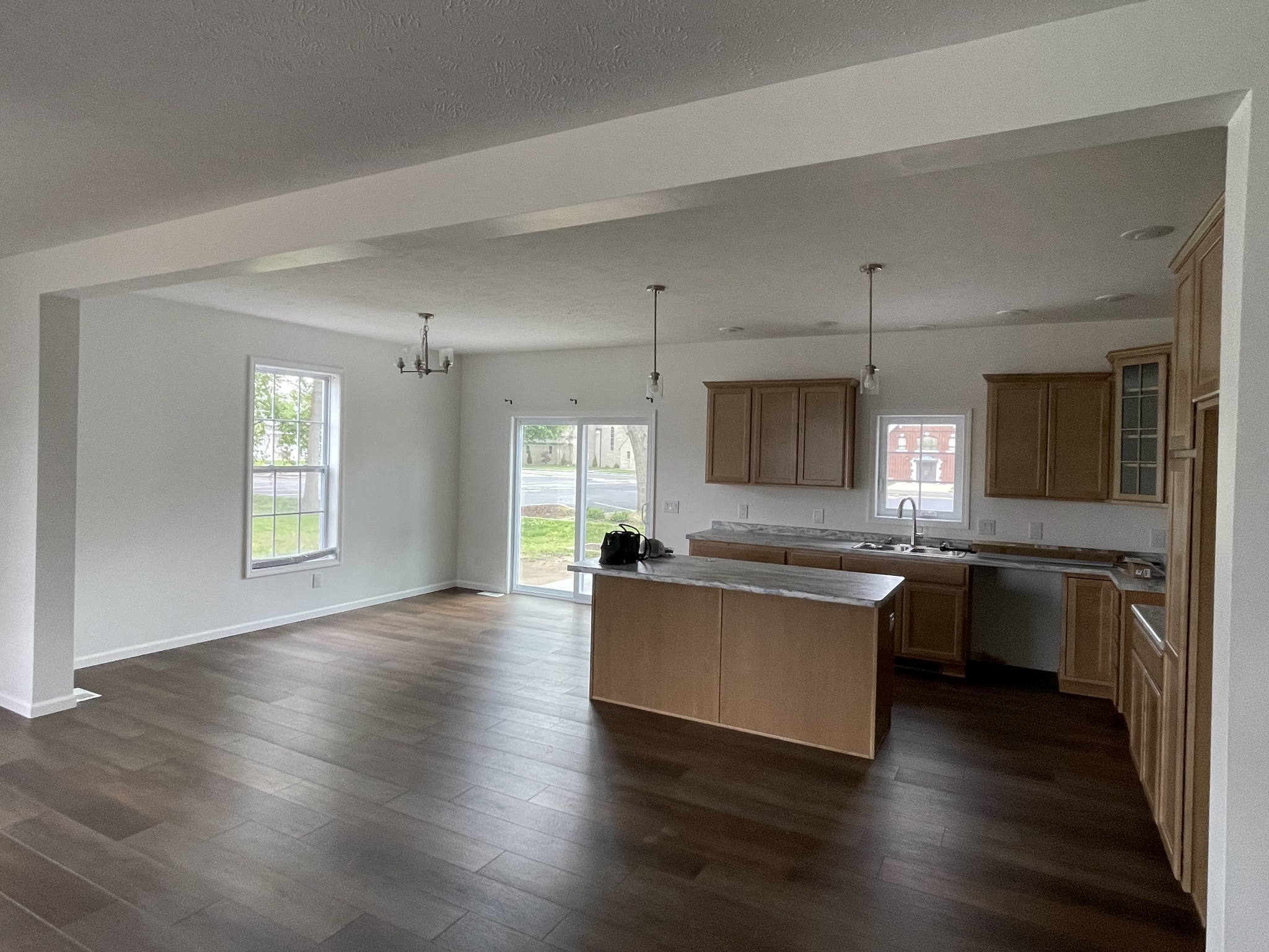 Open-concept kitchen and dining area in a modern home. Features light wood cabinets, an island, dark wood floors, and large windows, creating a bright and spacious feel.